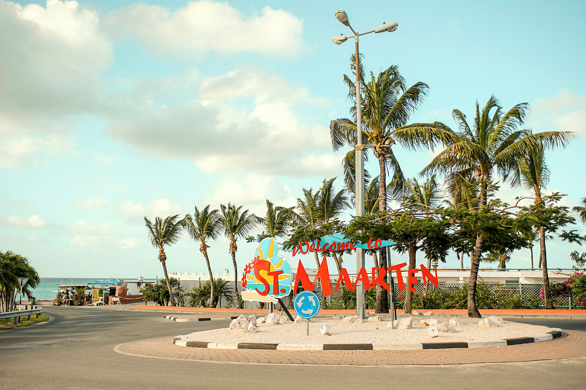 Skilt som sier "Welcome to St. Maarten" omgitt av palmer. (AI-generert tekst)
