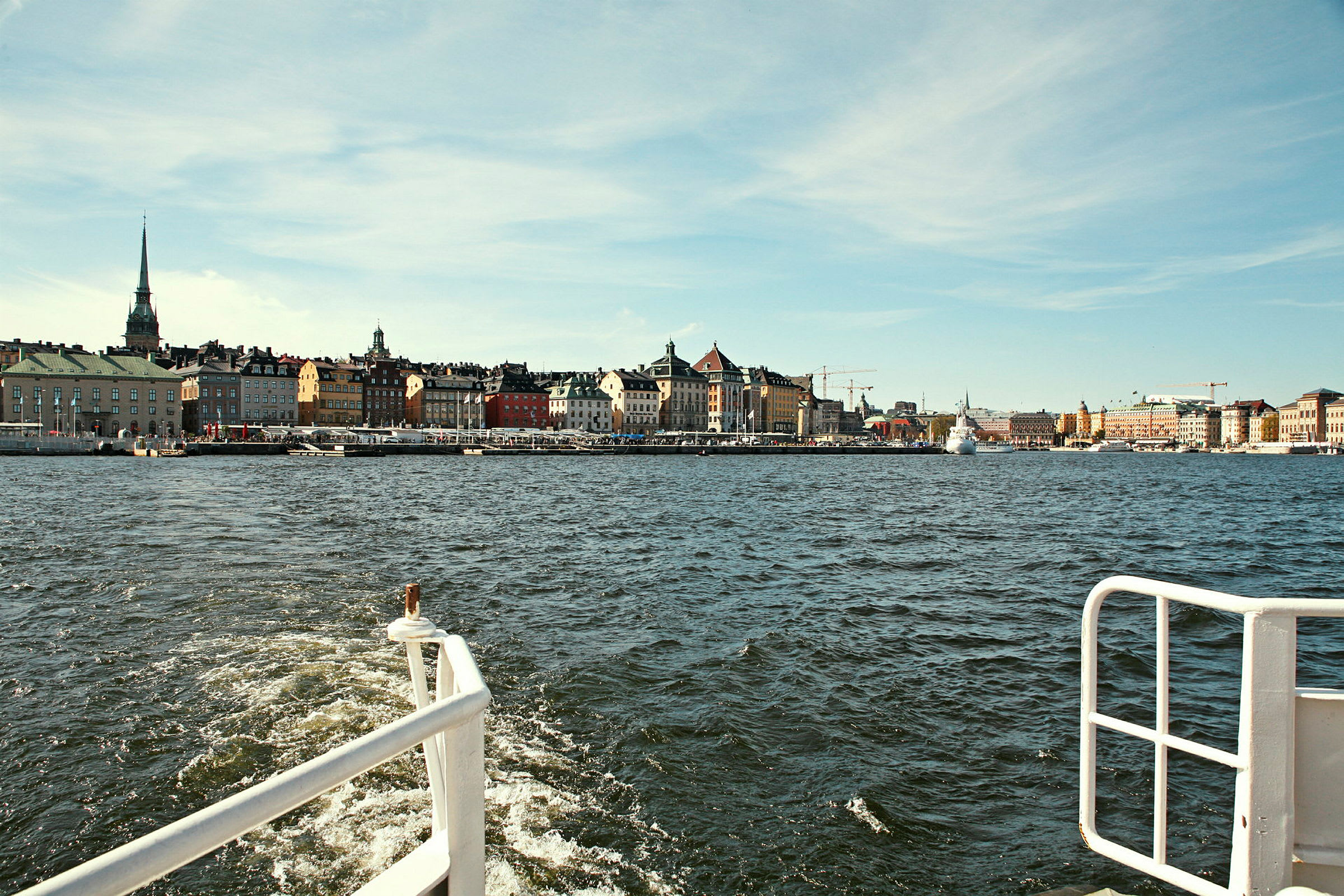 Utsikt fra en båt med en bypromenade og fargerike bygninger langs vannet. (AI-generert tekst)