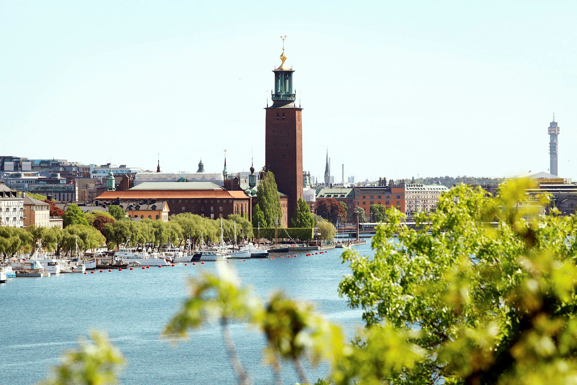 En stor bygning som står ved en vannkant, med grøntområder og seilbåter i forgrunnen. (AI-generert tekst)