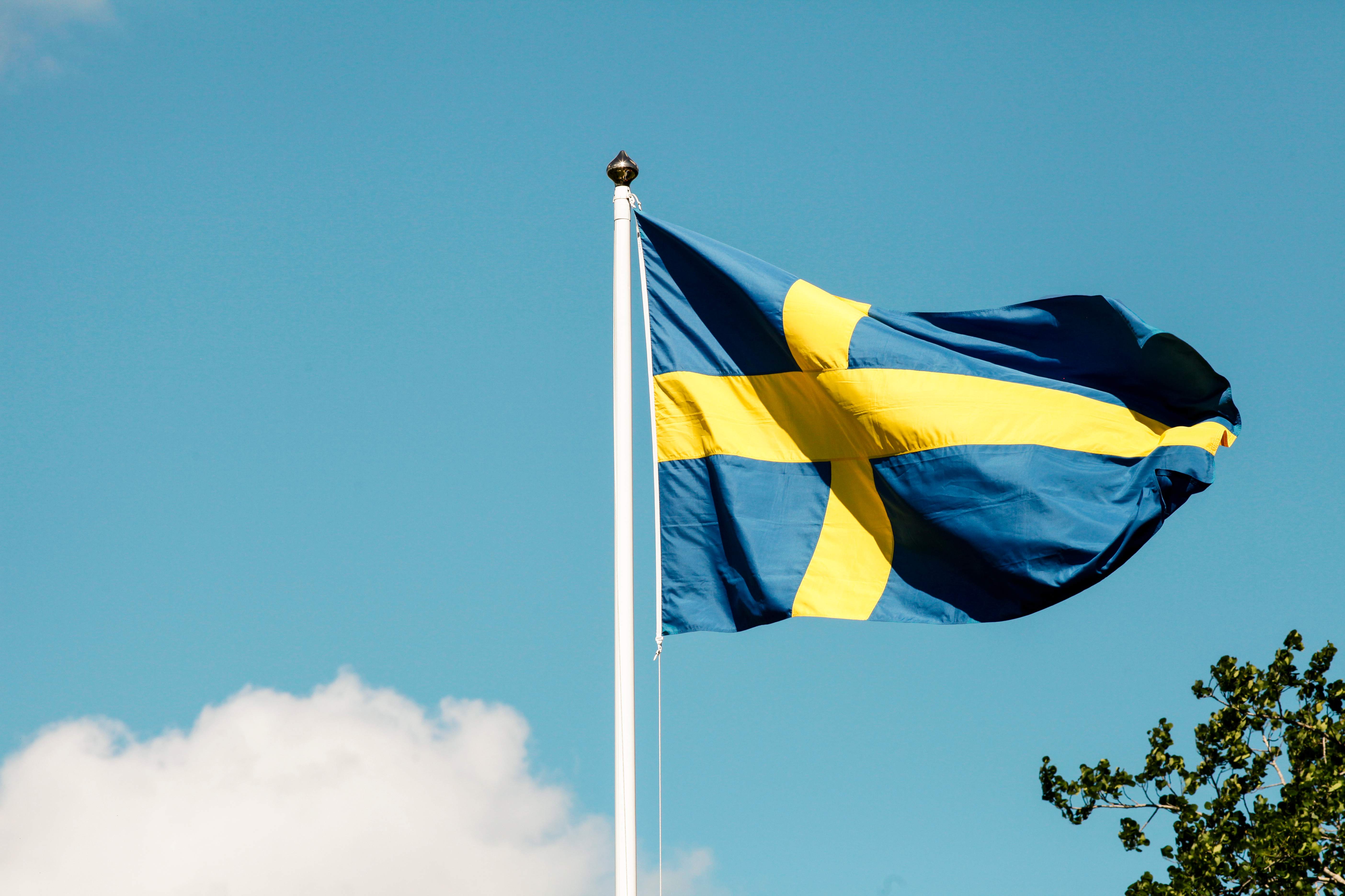 Et svensk flagg vaier mot en blå himmel med hvite skyer. (AI-generert tekst)