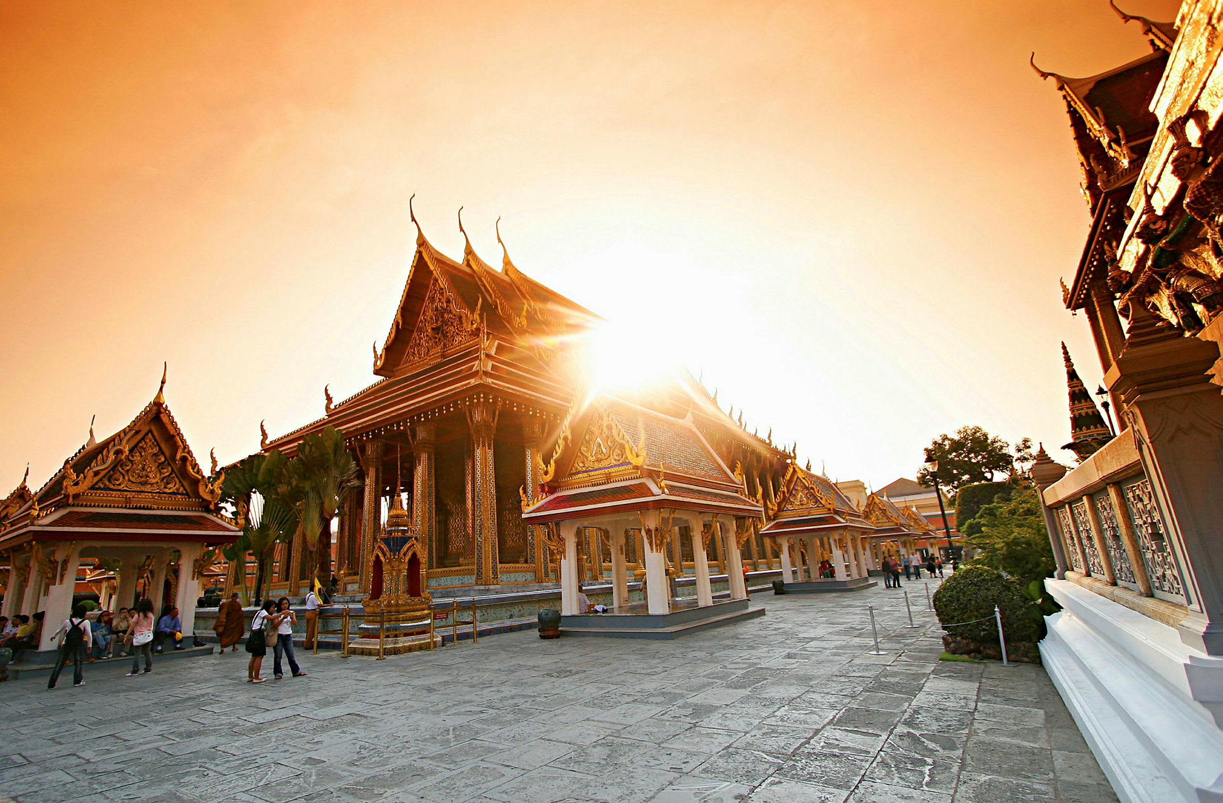 Bildet viser et thailandsk tempel med dekorerte tak og bygninger i solnedgangens lys. (AI-generert tekst)