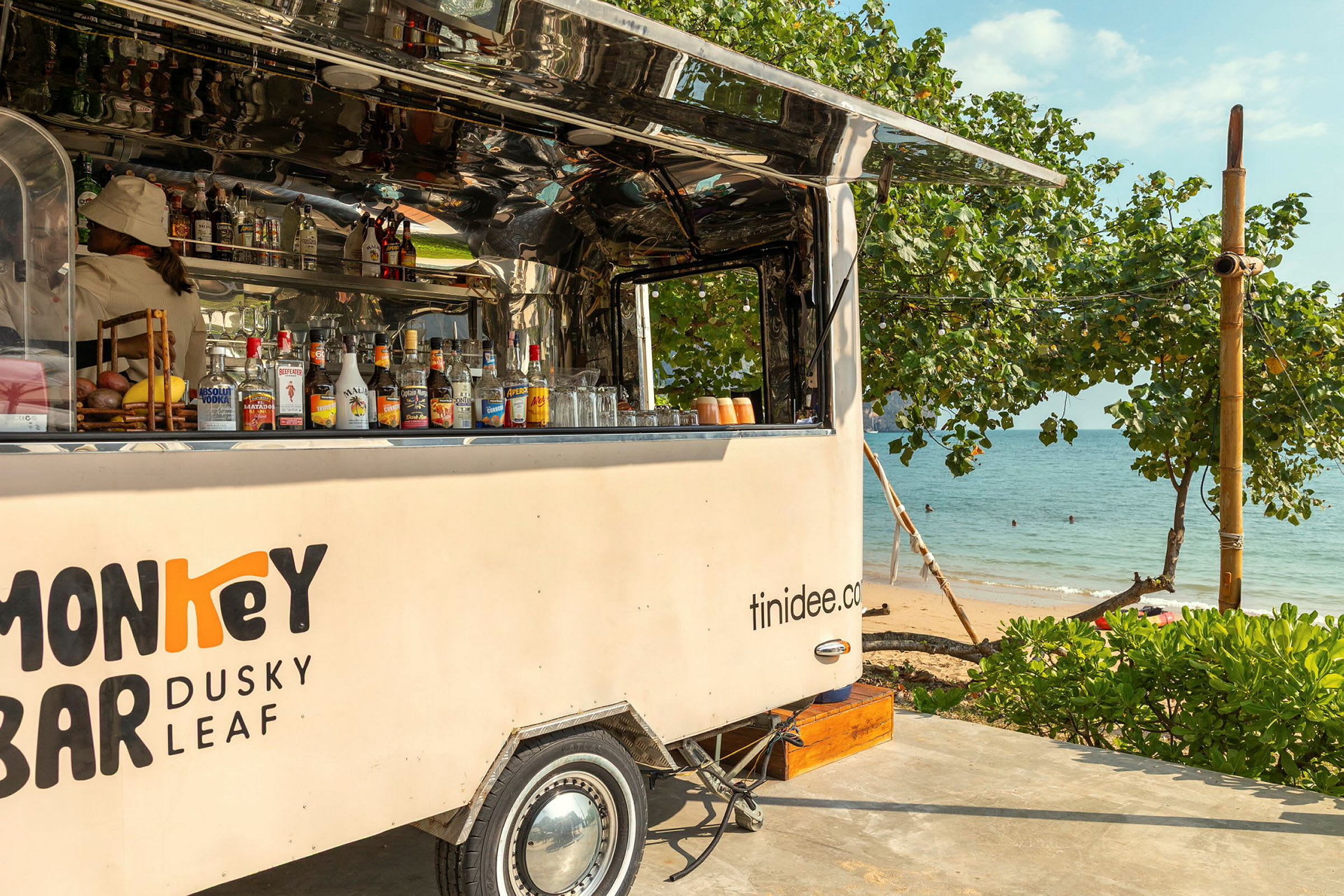 Mobil bar oppstilt ved stranden, omgitt av grøntområder og hav i bakgrunnen. (AI-generert tekst)