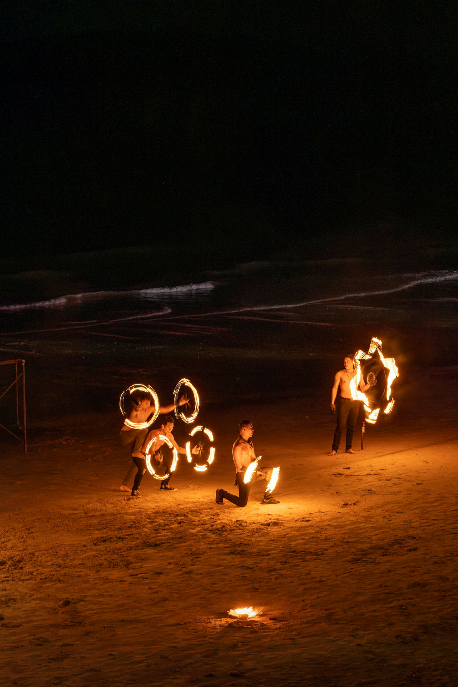 Personer utfører et ildshow på en sandstrand om natten. (AI-generert tekst)
