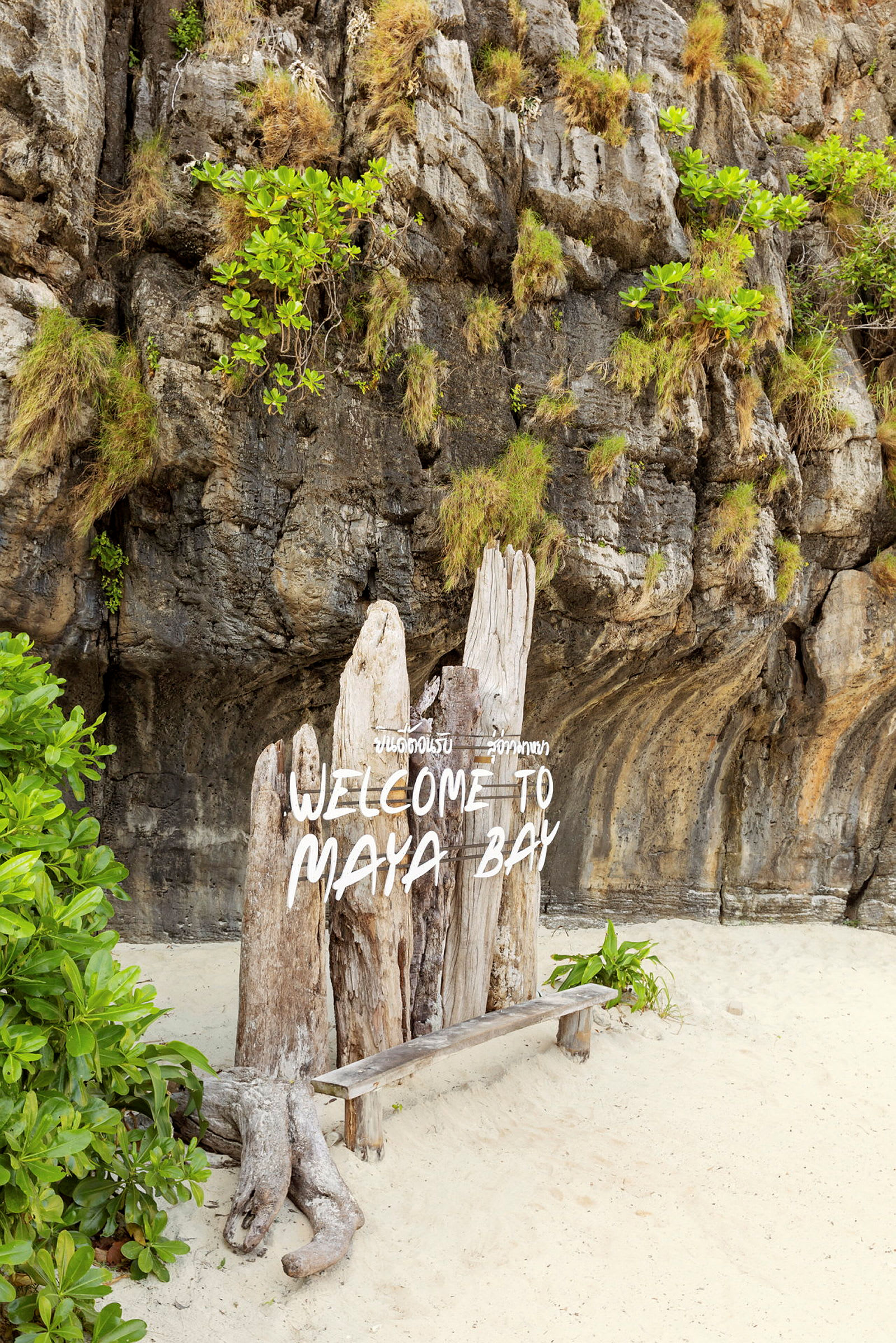 Skilt med teksten 'Welcome to Maya Bay' foran en klippevegg og en sandstrand. (AI-generert tekst)