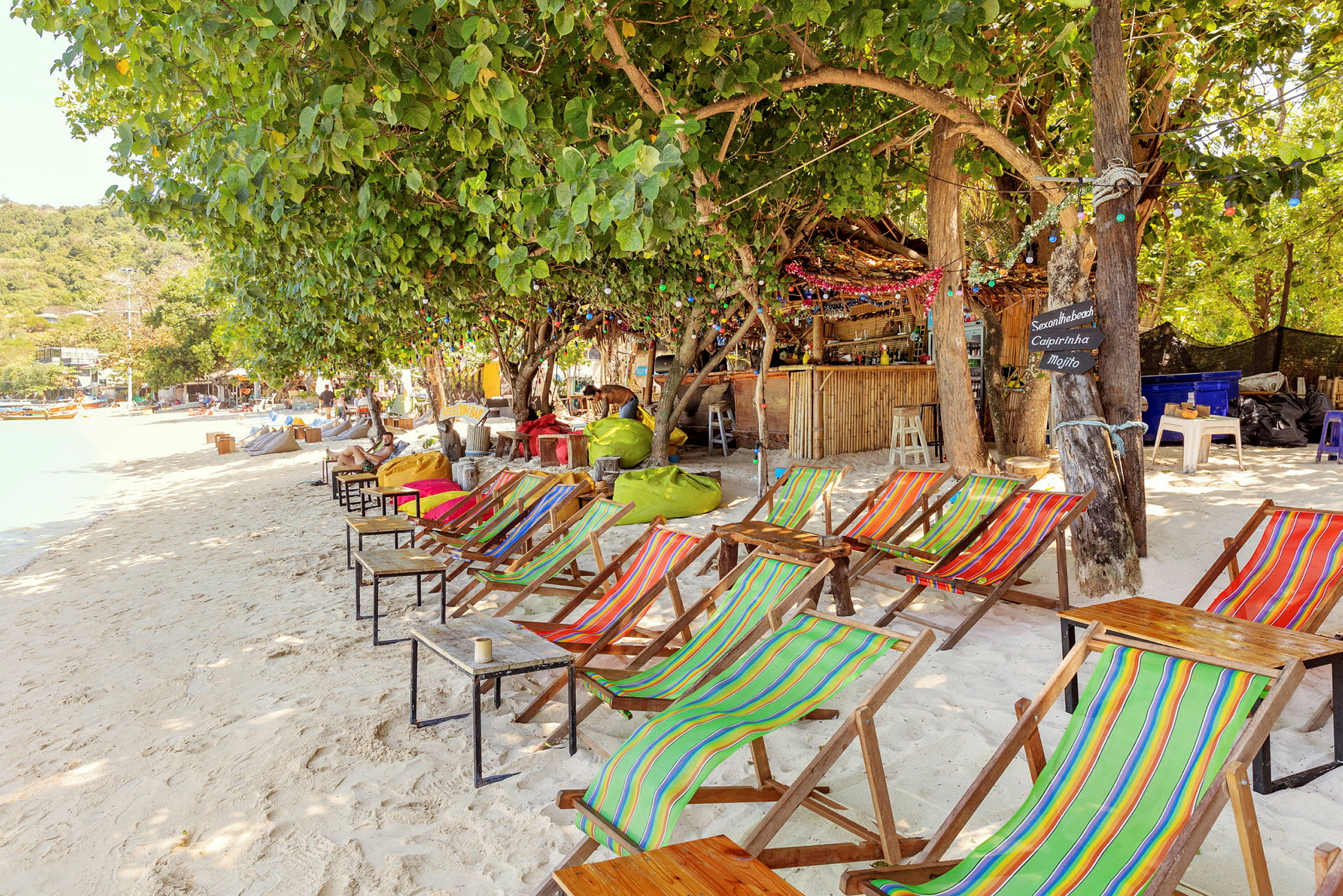 Strand med fargerike solsenger og et trekantet kafé i bakgrunnen. (AI-generert tekst)