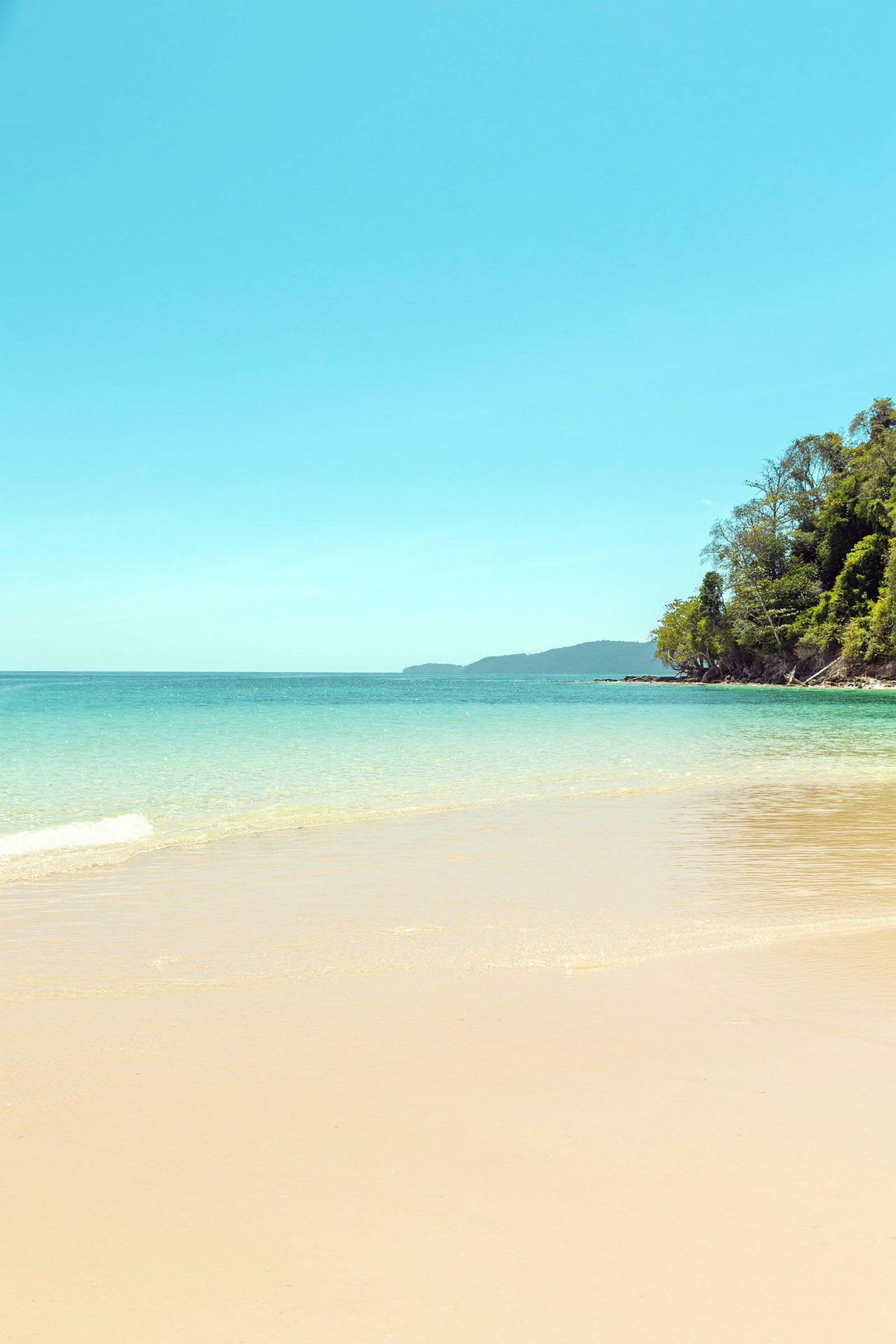 Bilde av en strand med klart vann, frodig vegetasjon langs kysten og en blå himmel. (AI-generert tekst)