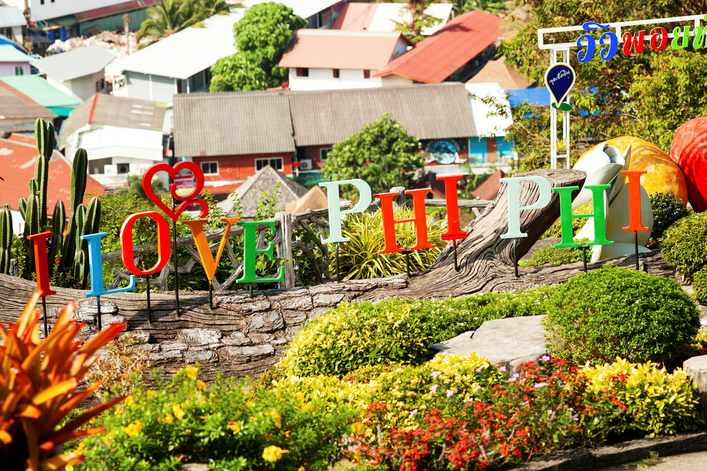 Fargerike bokstaver som staver "I Love Phi Phi" er satt i et hageområde med busker og blomster. (AI-generert tekst)