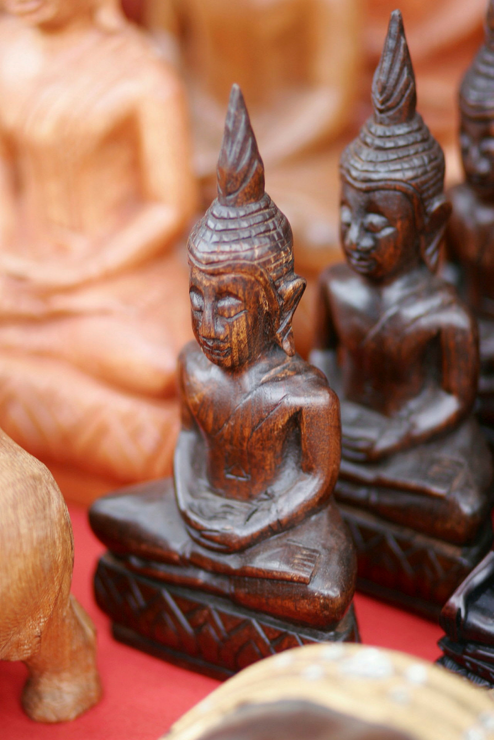Bilde av en samling små, treutskårne buddhastatuer foran en rød bakgrunn. (AI-generert tekst)