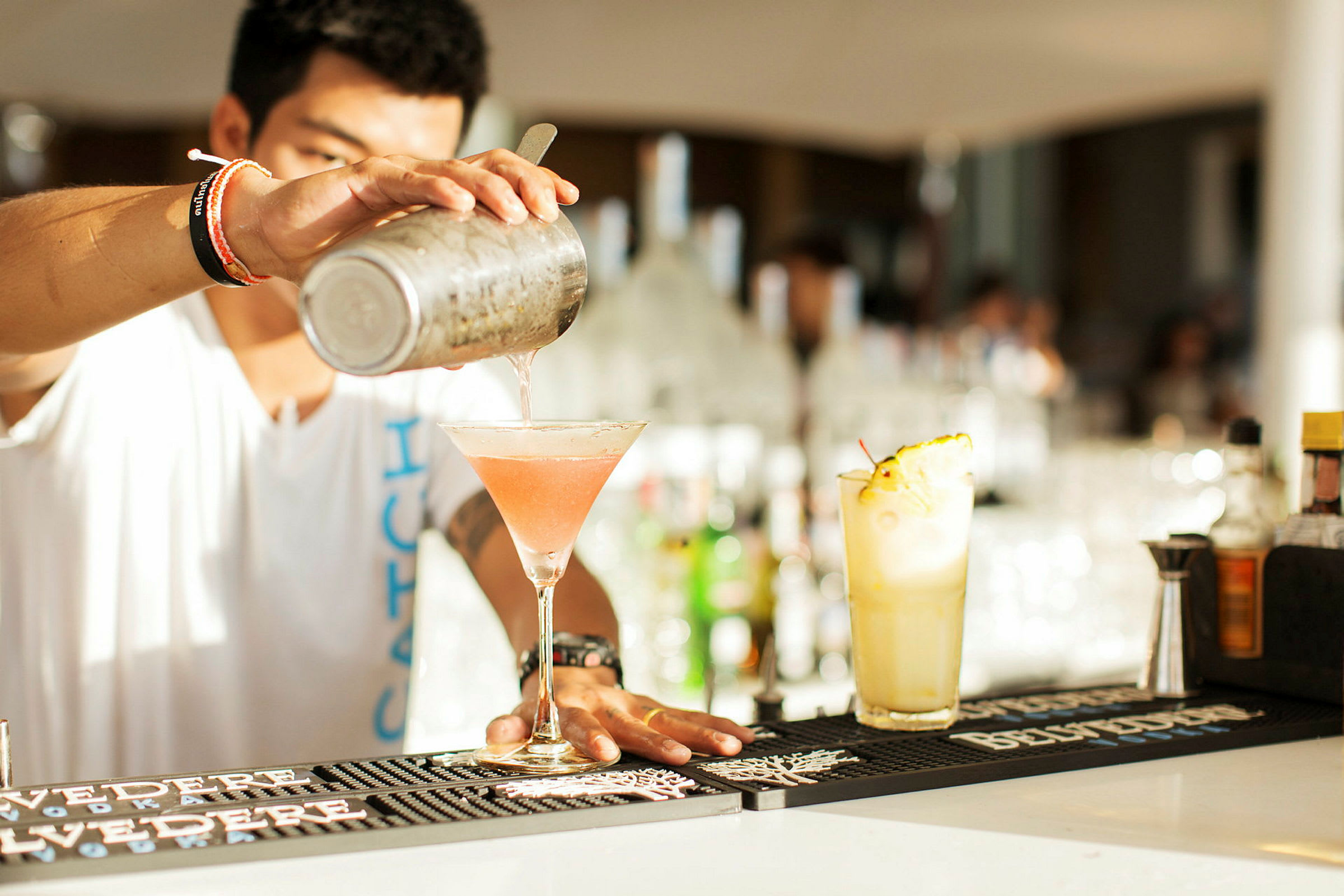 En cocktail blandes og helles i et glass på en bardisk. (AI-generert tekst)