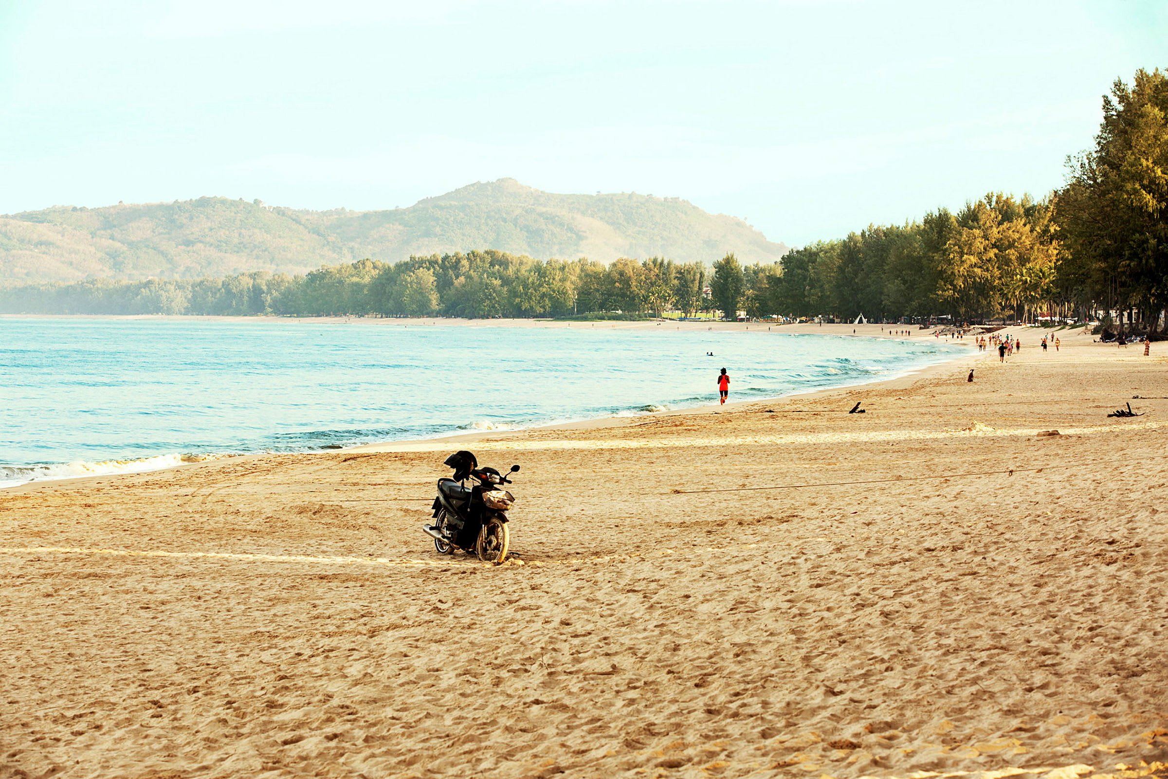 En strand med sand, havet og en motorsykkel. En person går nær vannet. (AI-generert tekst)