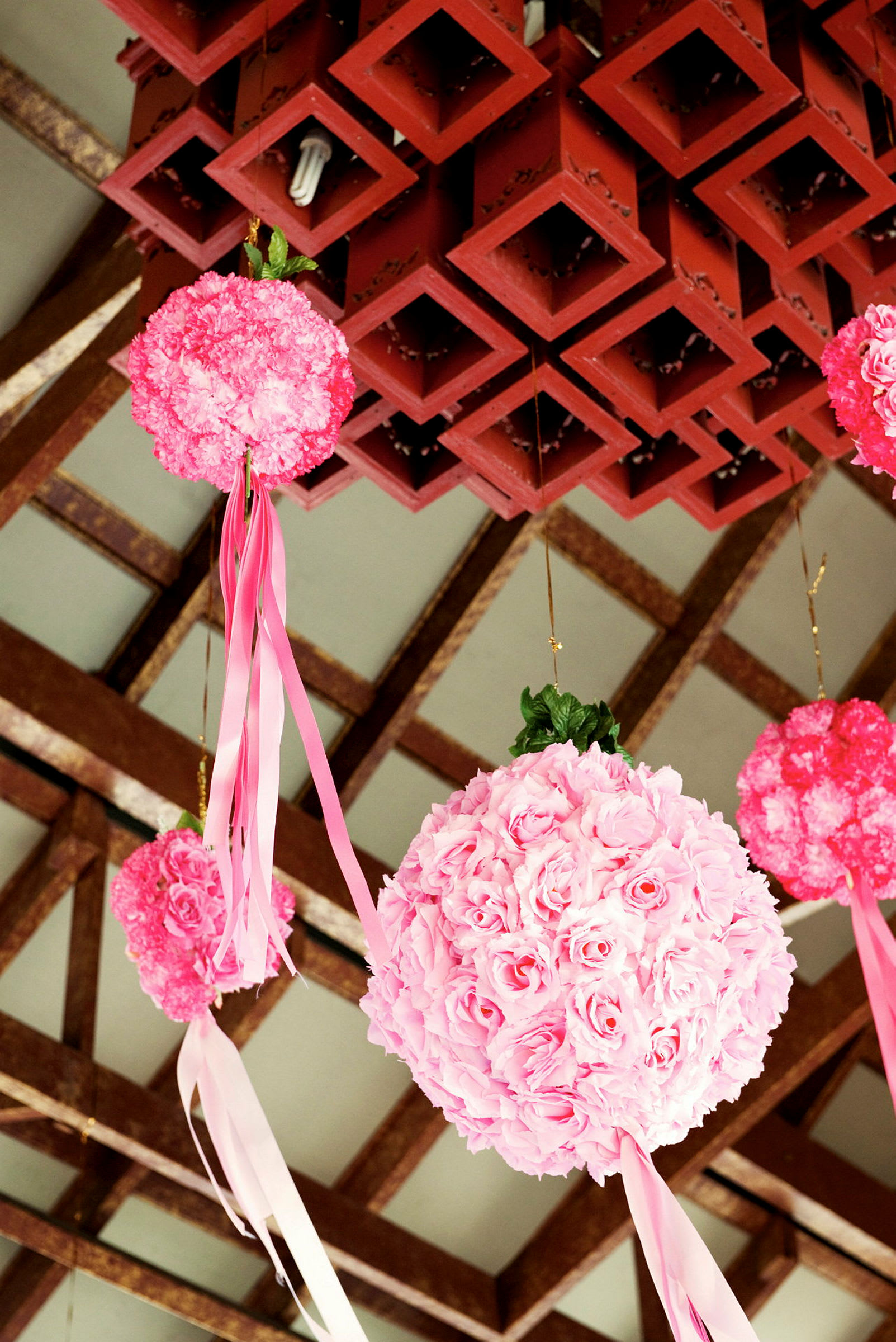 Dekorative kuler med rosa blomster og hengende bånd i rosa og hvite farger, hengende fra en takstruktur. (AI-generert tekst)