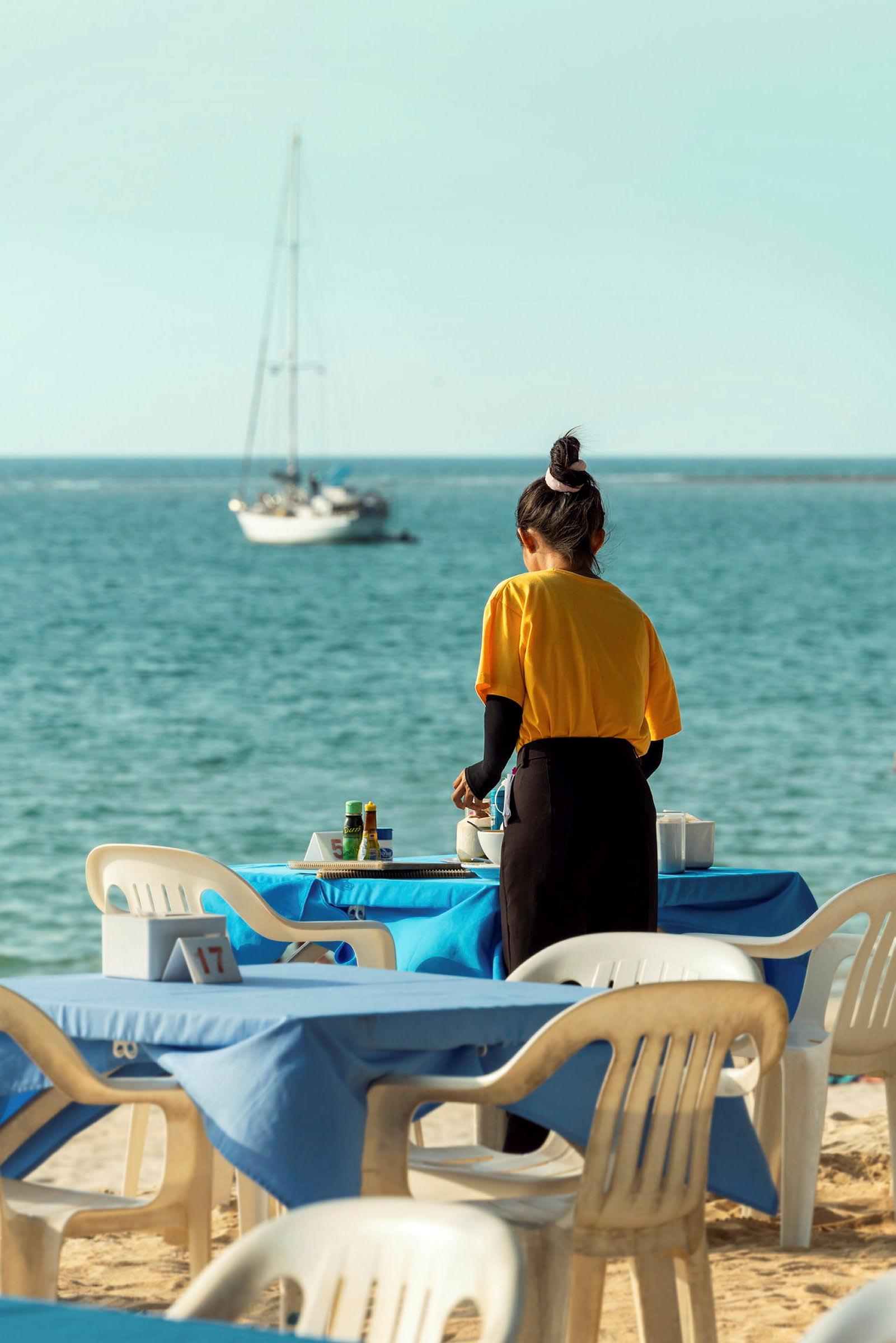 En person ordner bord på en restaurant med utsikt over havet. (AI-generert tekst)