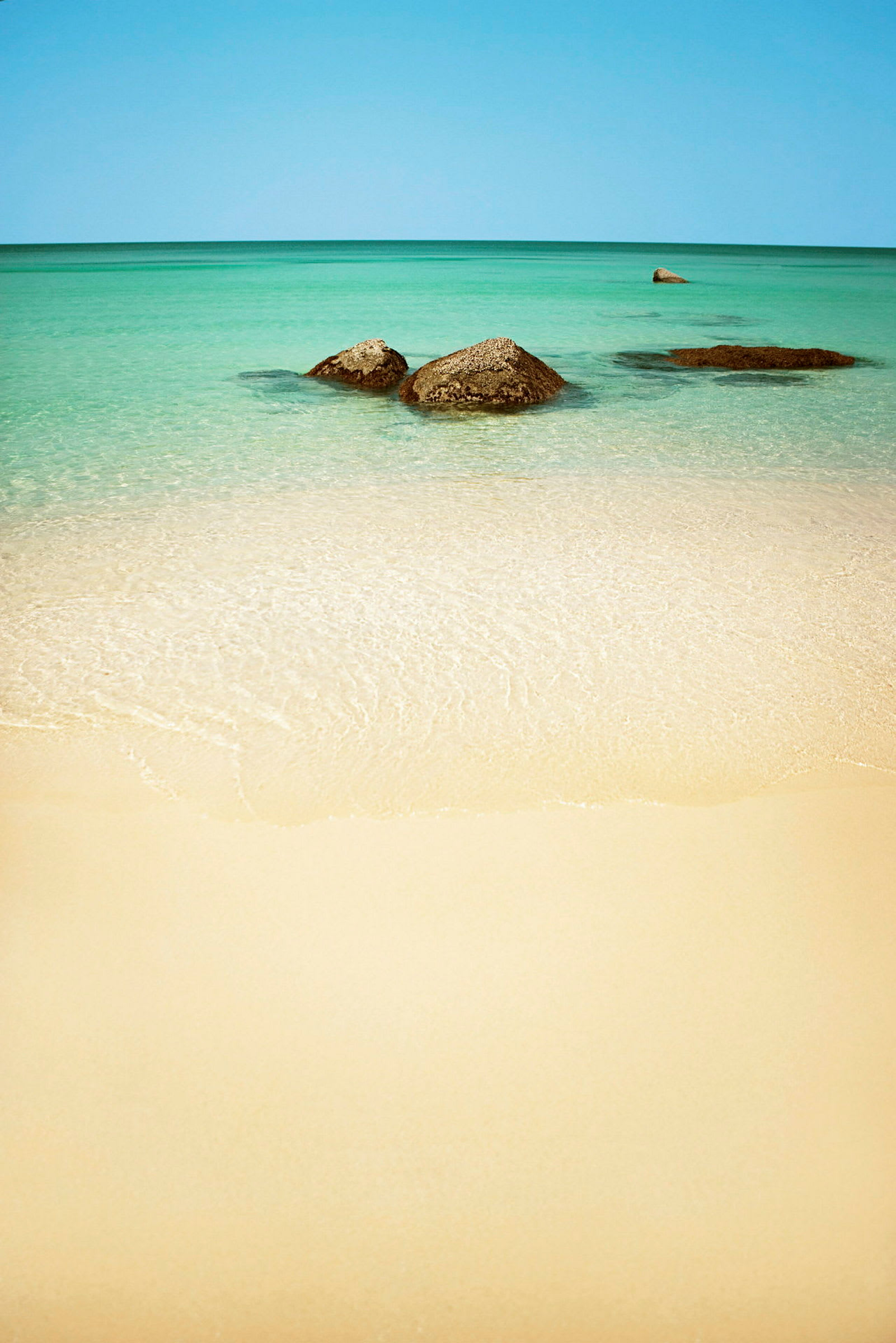 En sandstrand med klart vann og noen synlige steiner i havet. (AI-generert tekst)