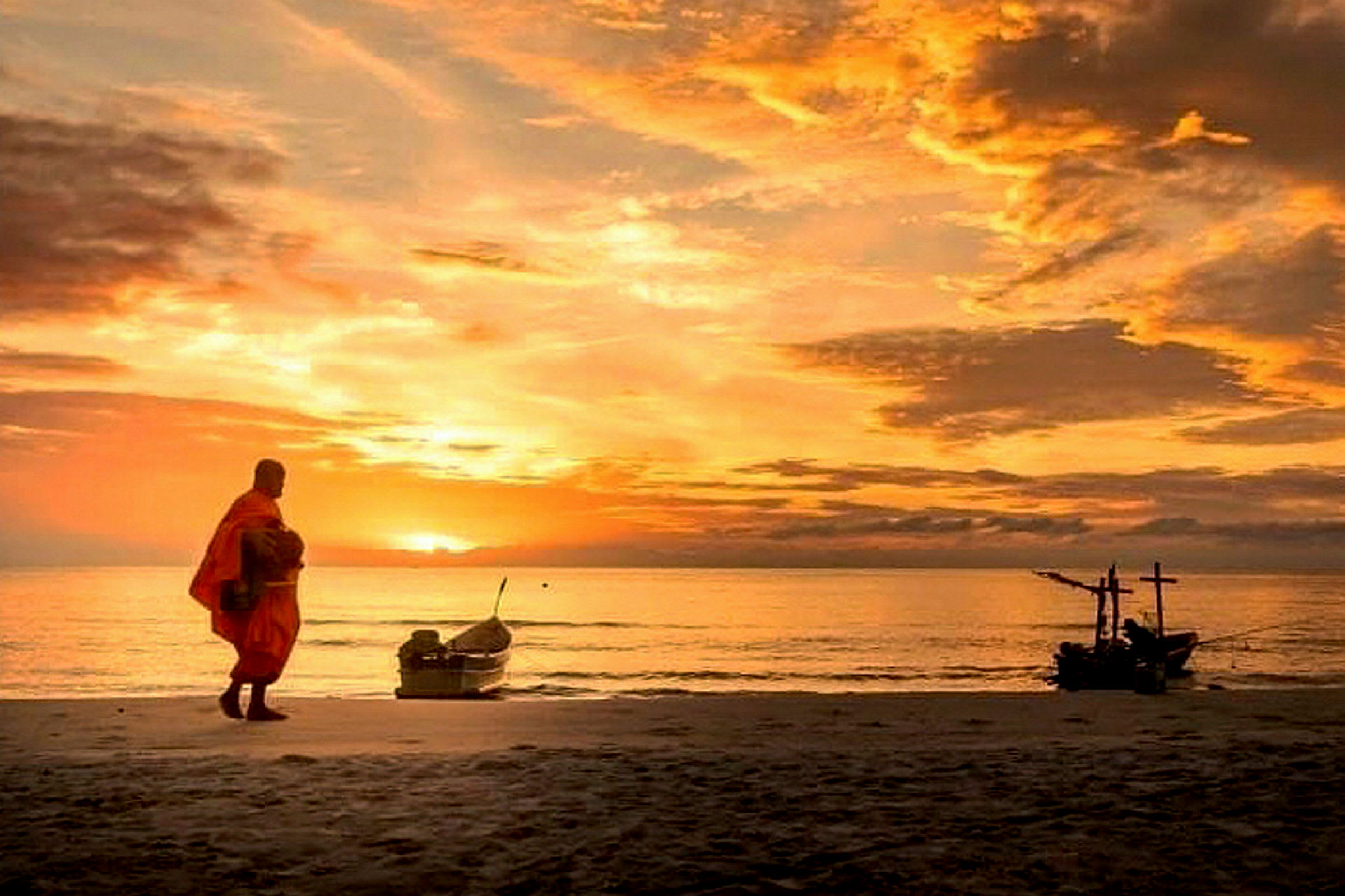 Bilde av en person i oransje klær som går på en strand ved solnedgang. En båt er synlig på vannet. (AI-generert tekst)