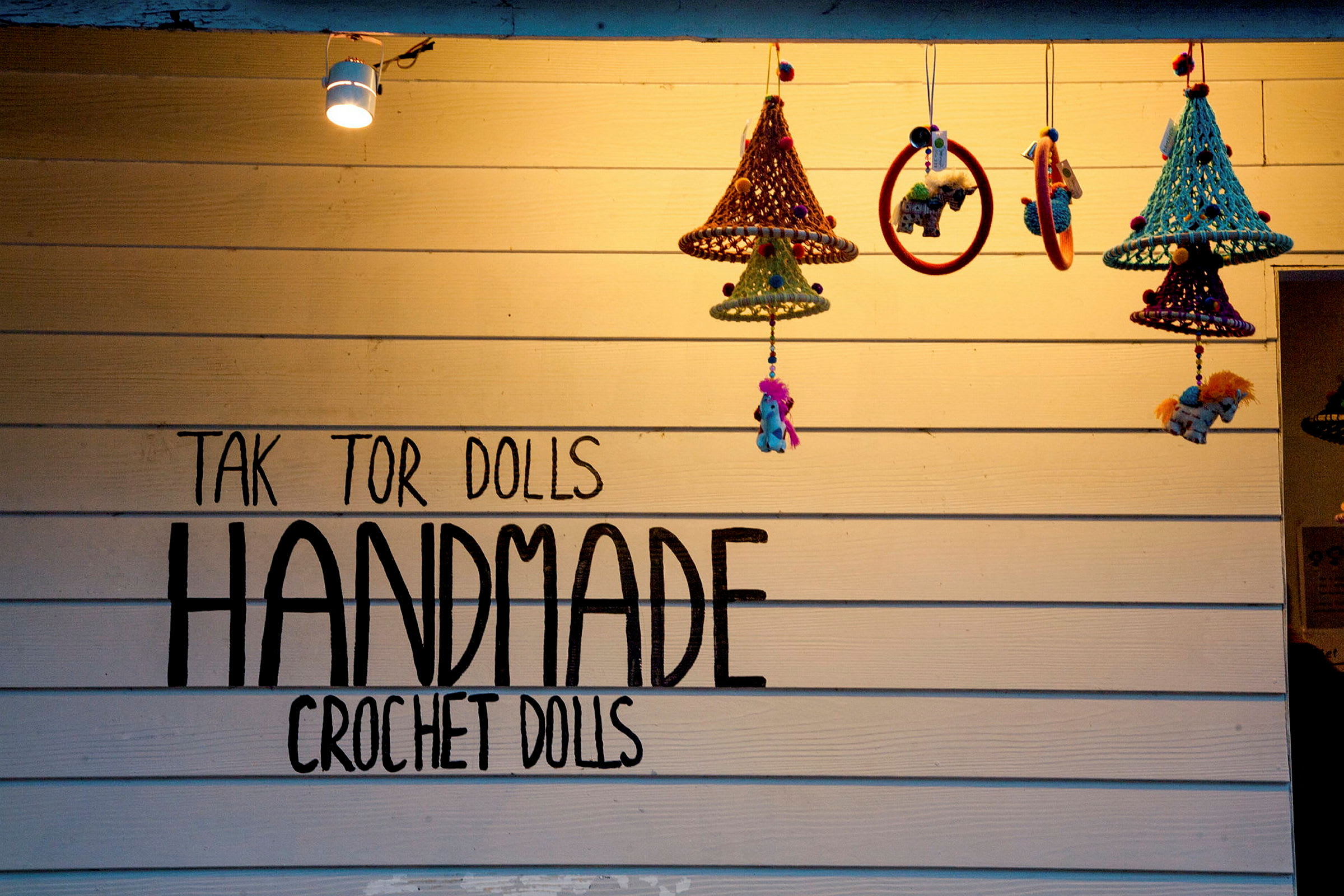 Vegg med teksten 'Handmade Crochet Dolls' og hengende heklede dekorasjoner. (AI-generert tekst)