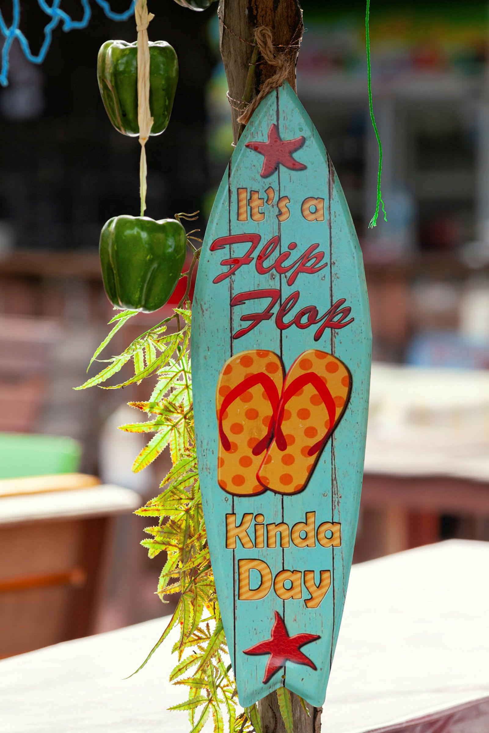 Et blått skilt med teksten 'It's a flip-flop kinda day', et bilde av sandaler og dekorert med stjerner henger ved siden av grønn paprika og grønne blader. (AI-generert tekst)