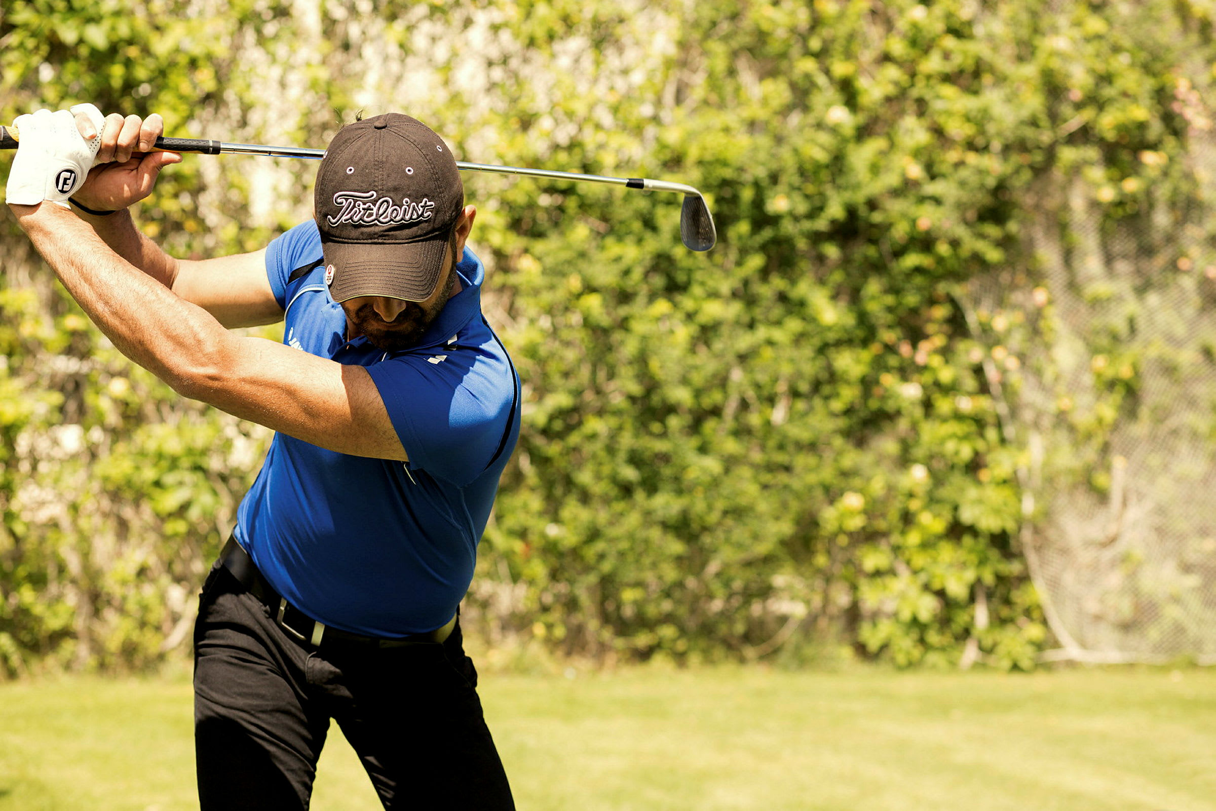 En mann i blå poloskjorte svinger en golfkølle på en gressplen. (AI-generert tekst)