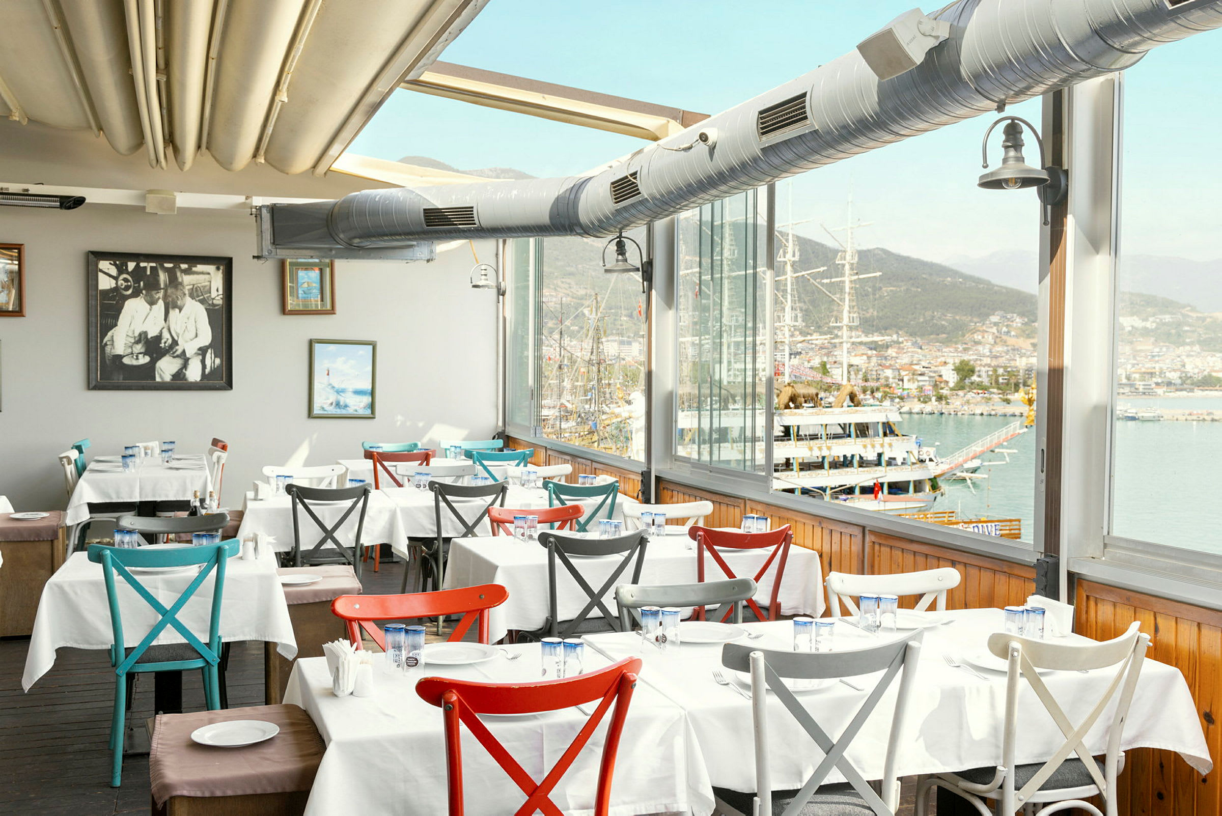 Interiør av en restaurant med dekkede bord og utsikt over havnen. (AI-generert tekst)