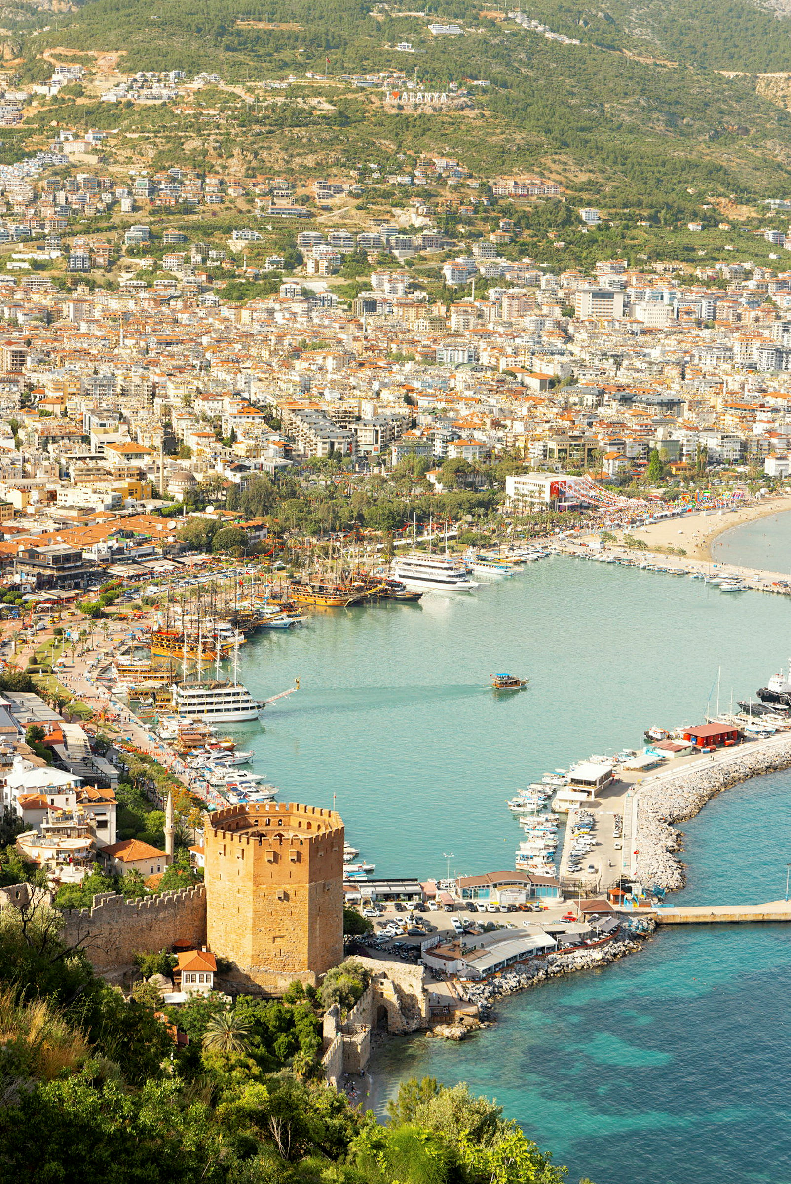 Utsikt over havn og byen Alanya med en historisk rød bygning i forgrunnen. (AI-generert tekst)