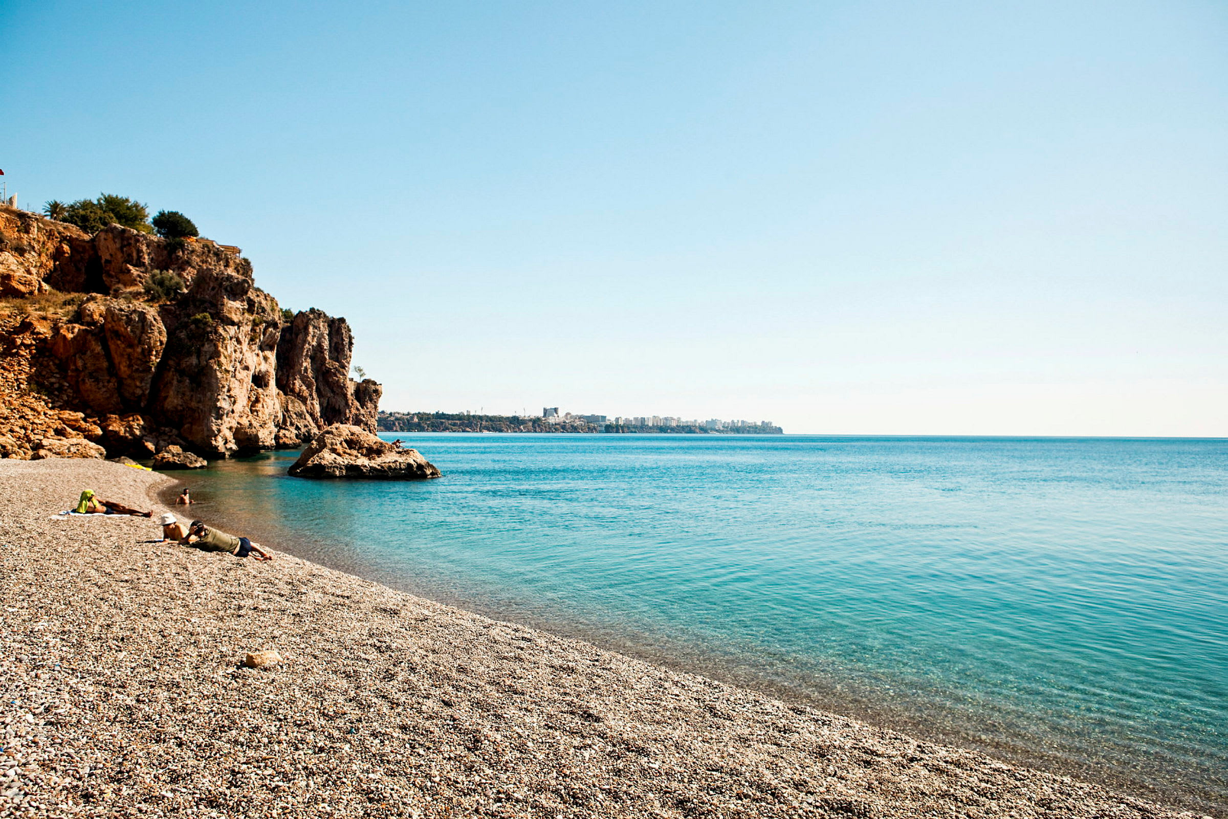 Sandstrand med klipper ved havet under klar himmel. (AI-generert tekst)