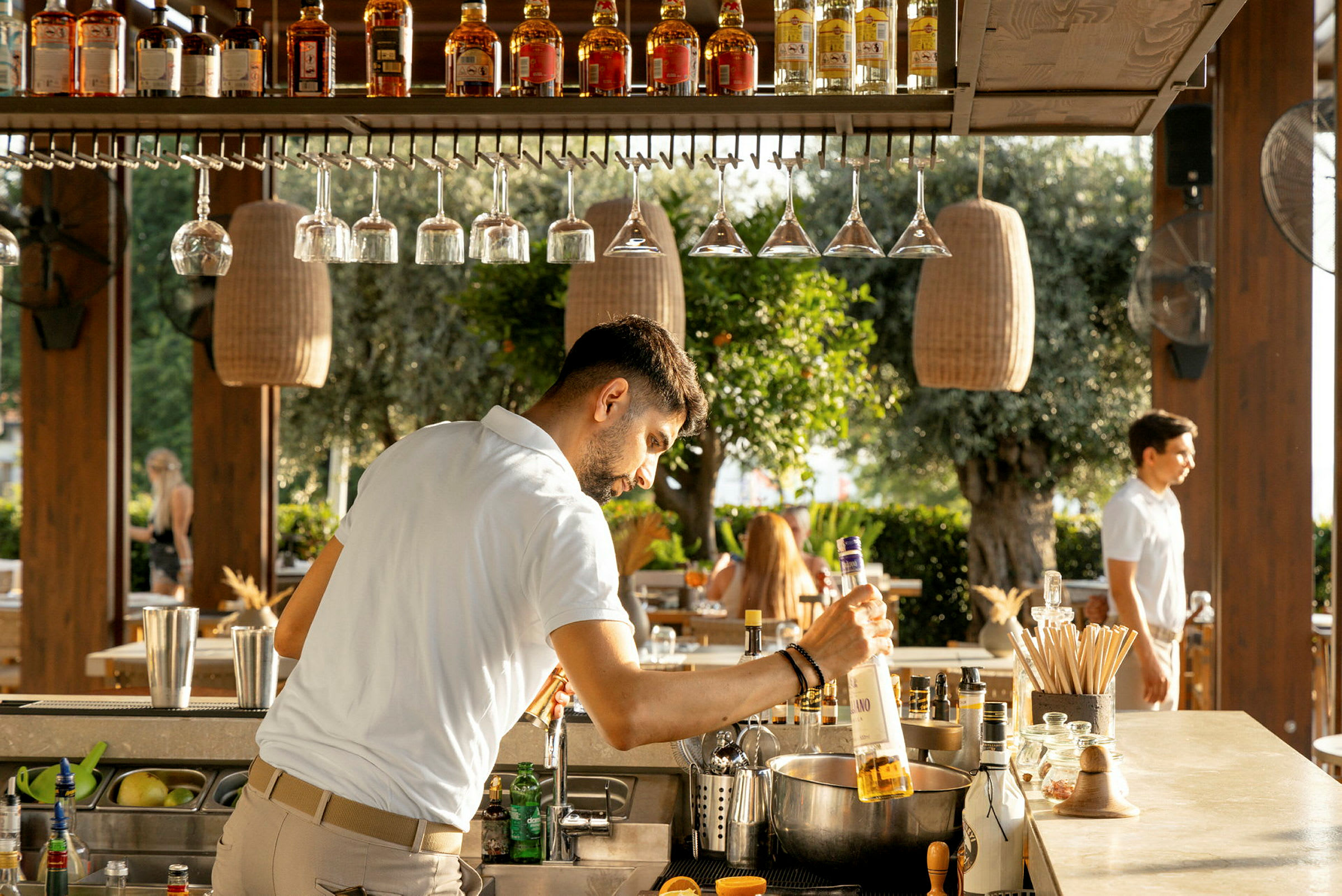 En bartender ved en utendørsbar strekker seg etter en flaske brennevin. (AI-generert tekst)