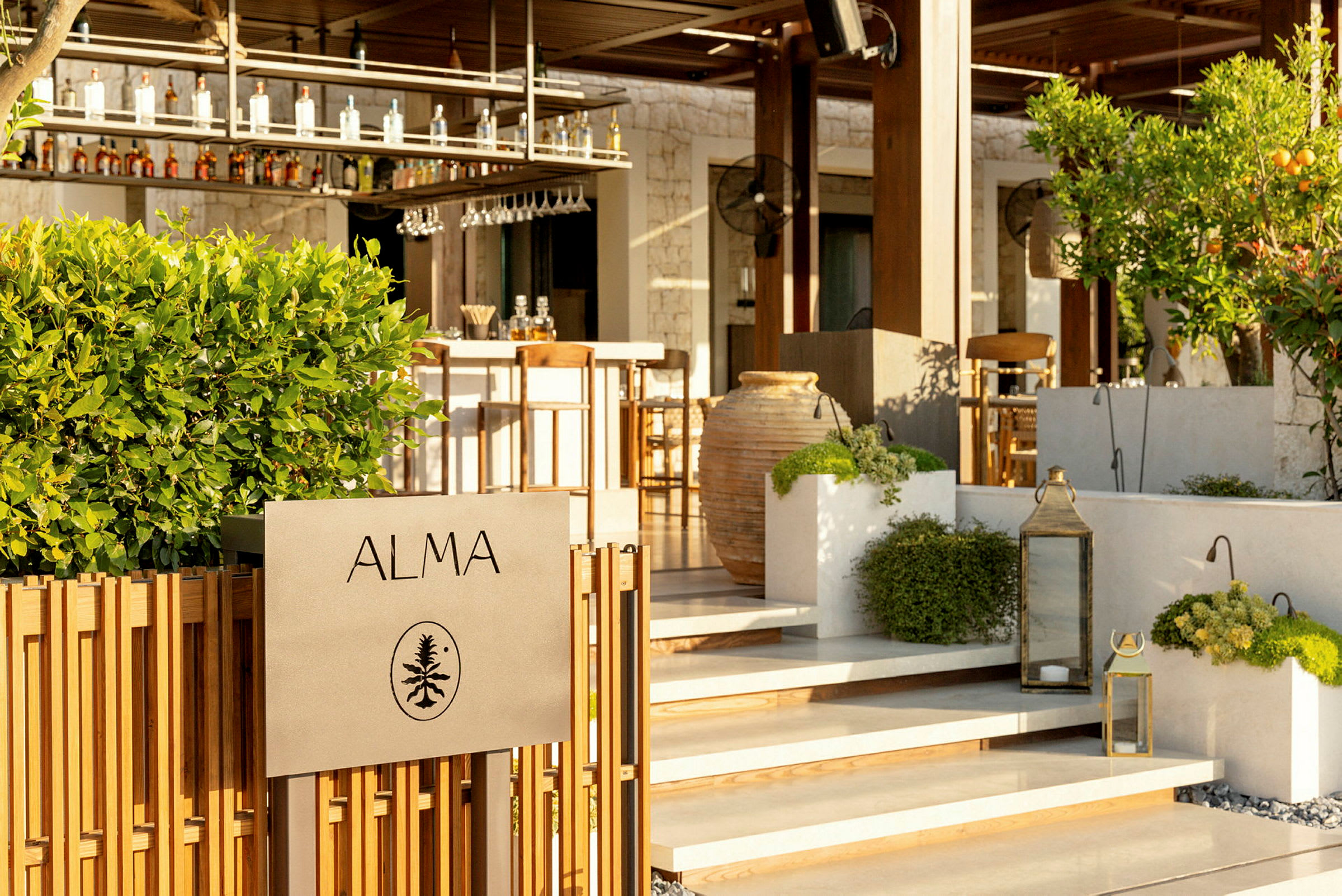 Skilt med teksten "ALMA" foran en bar med grøntområder og dekorasjoner. (AI-generert tekst)