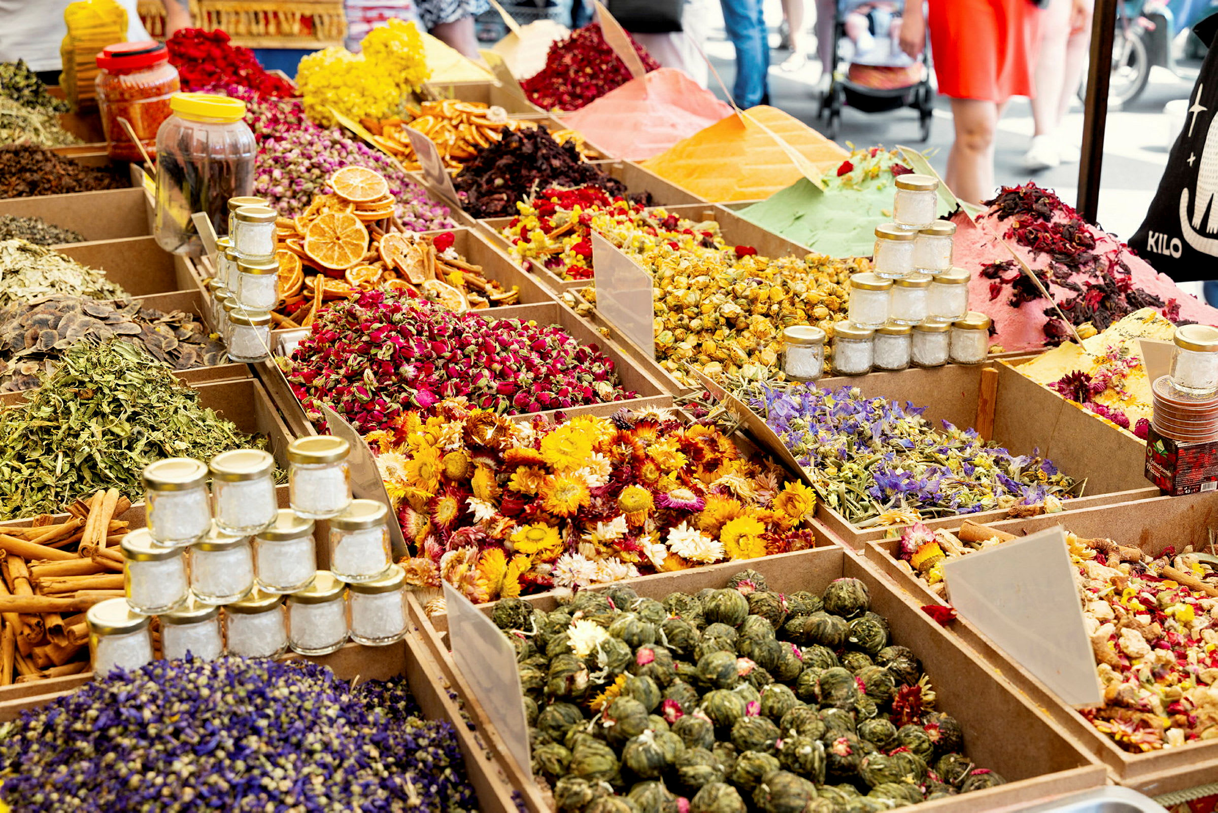 En markedsplass med fargerike krydder, tørkede blomster og urteblandinger i bokser. (AI-generert tekst)