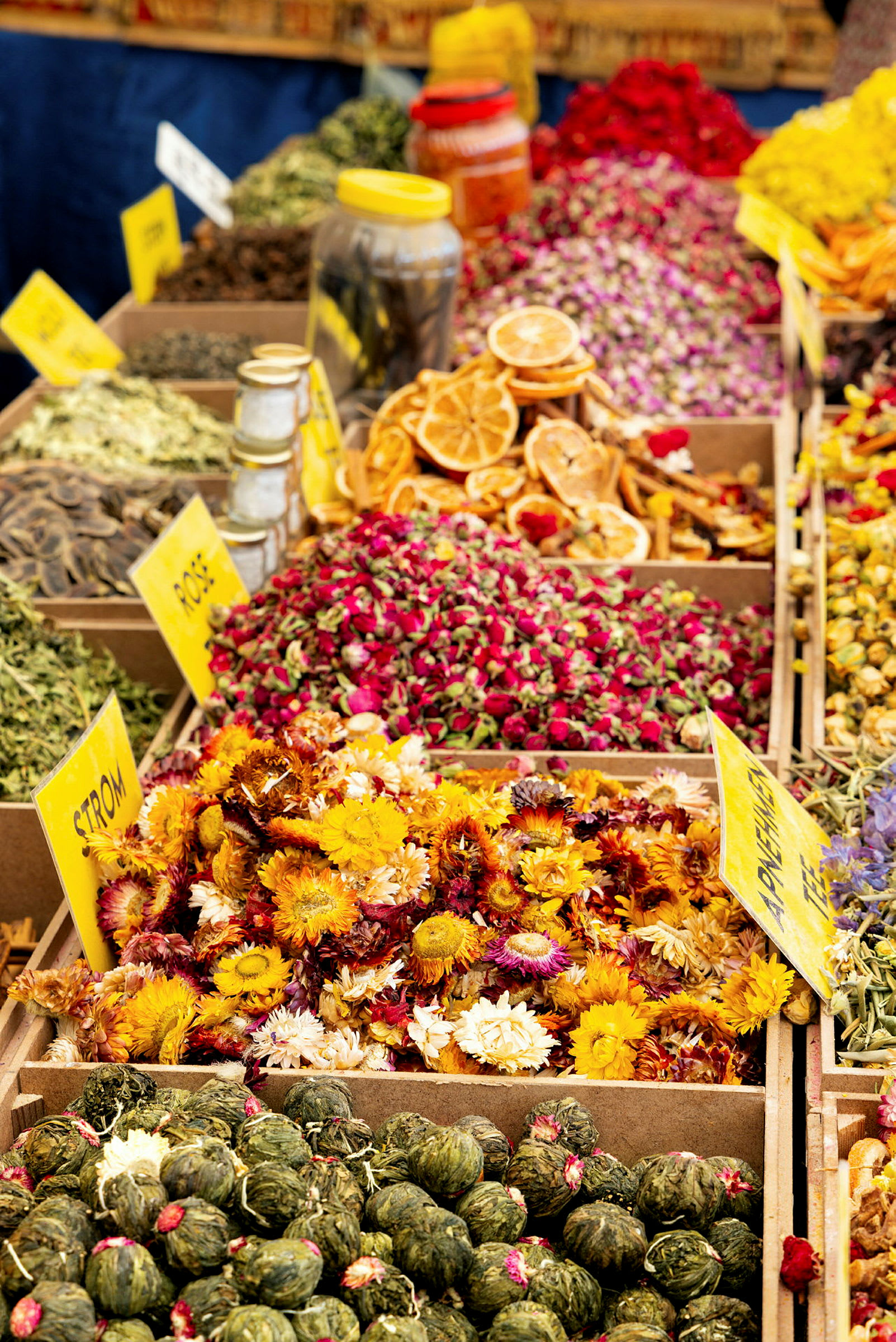Nærbilde av ulike krydder, urter og tørkede blomster i esker på et marked. (AI-generert tekst)