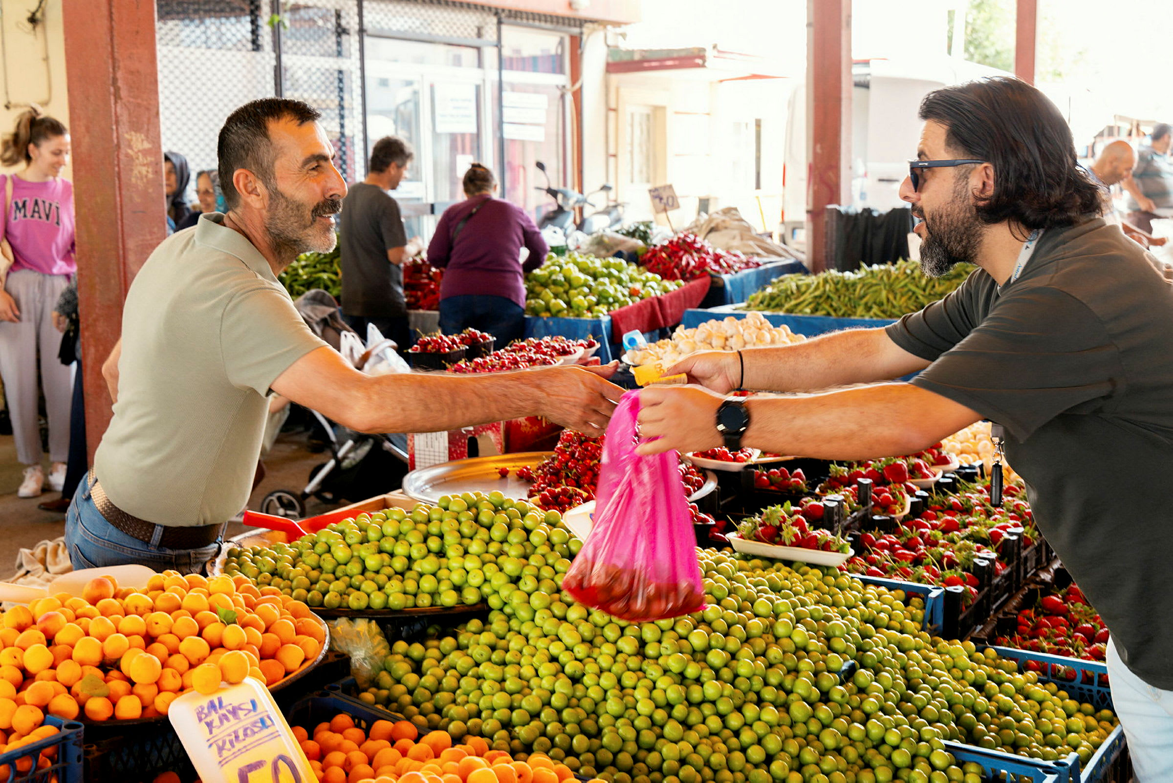 En markedsplass med forskjellige frukter og grønnsaker, og en kjøpsprosess hvor varer overrekkes. (AI-generert tekst)