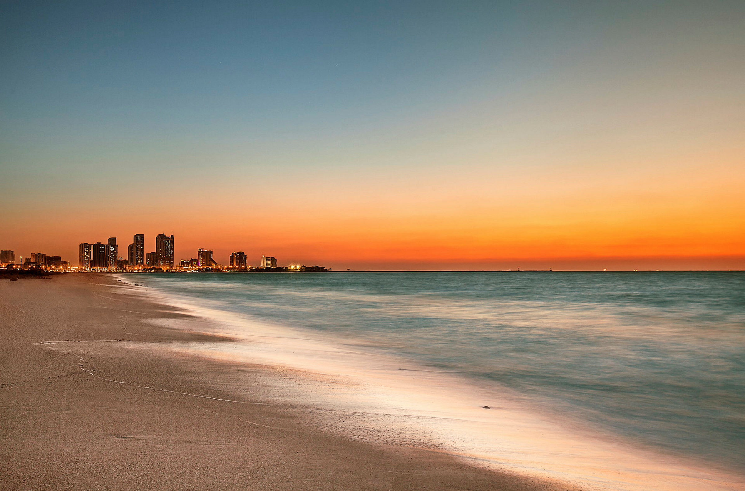 Byens skyline ved solnedgang, med havet og stranden i forgrunnen. (AI-generert tekst)