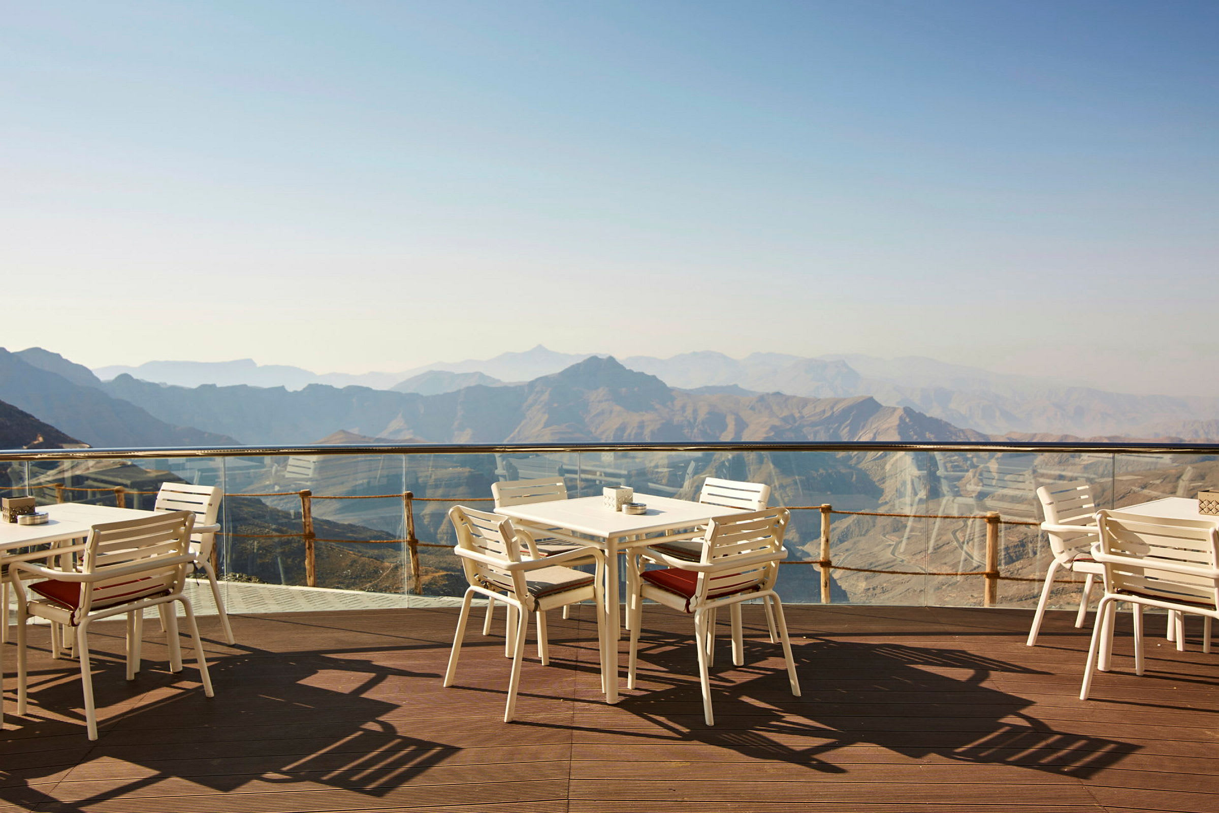 Utsikt over fjell fra en terrasse med hvite bord og stoler. (AI-generert tekst)