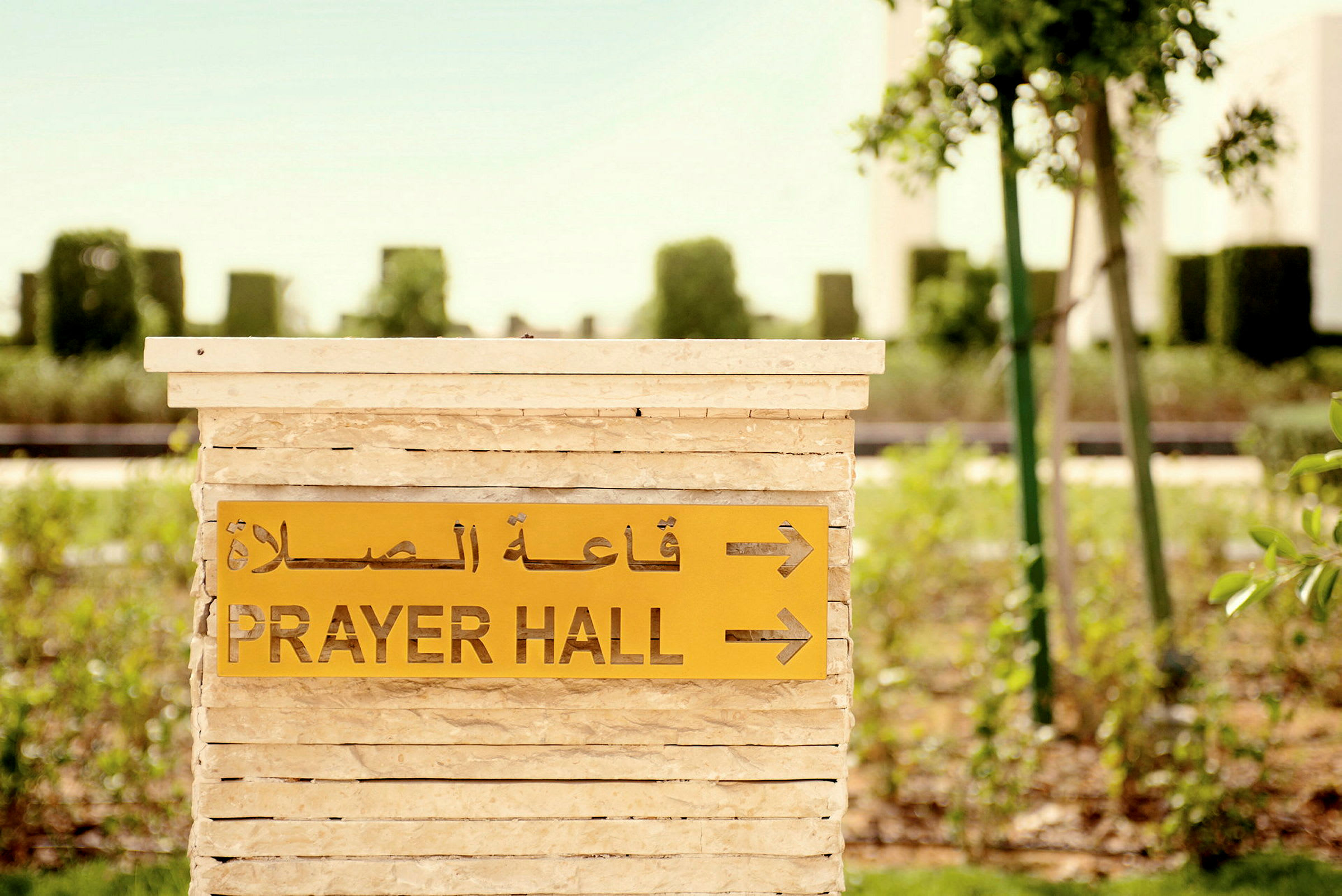 Et skilt med teksten 'Prayer Hall' og arabisk tekst peker mot en bønnshall, omgitt av grønt. (AI-generert tekst)