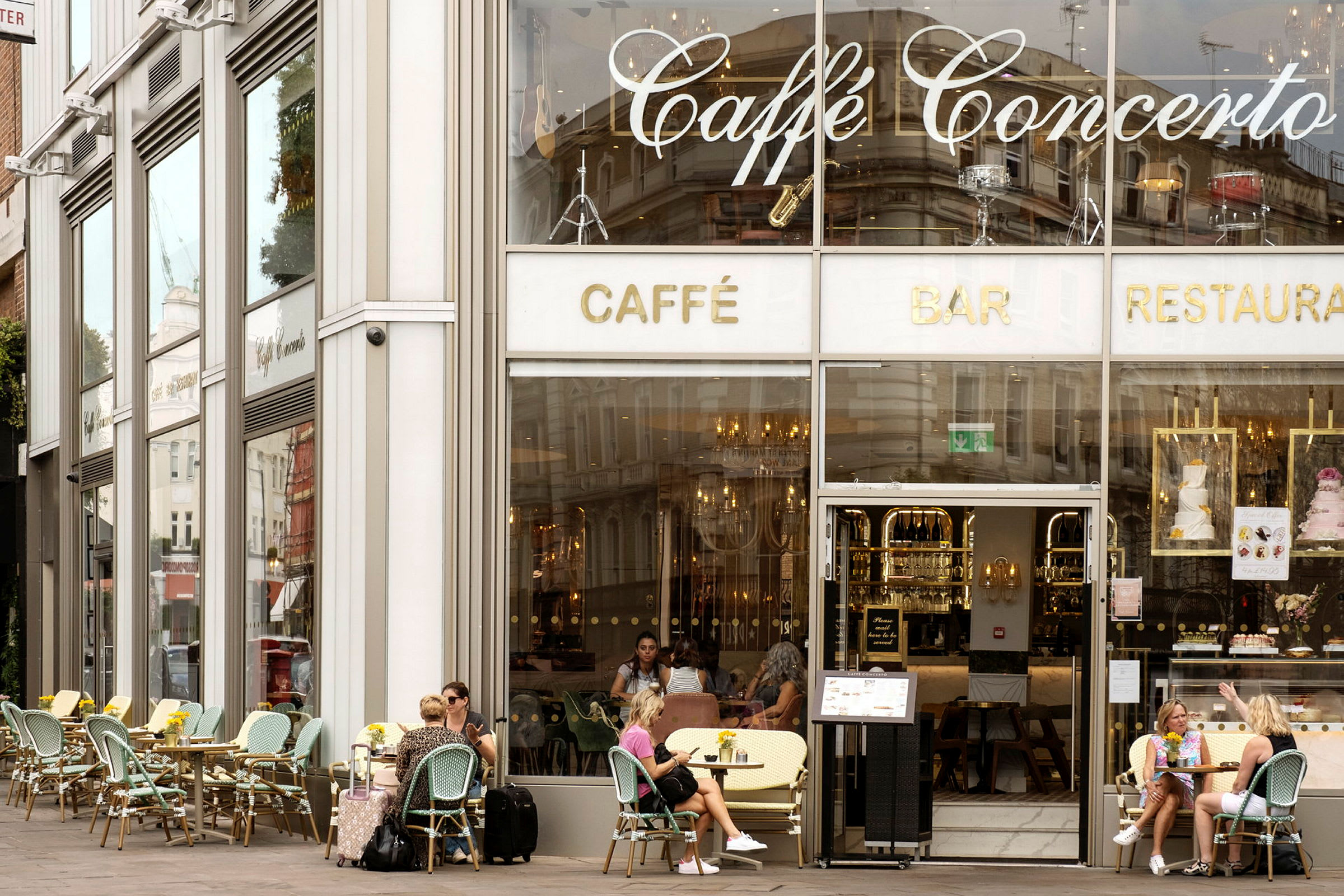 Fasaden til en kafé med store glassvinduer og uteservering. (AI-generert tekst)
