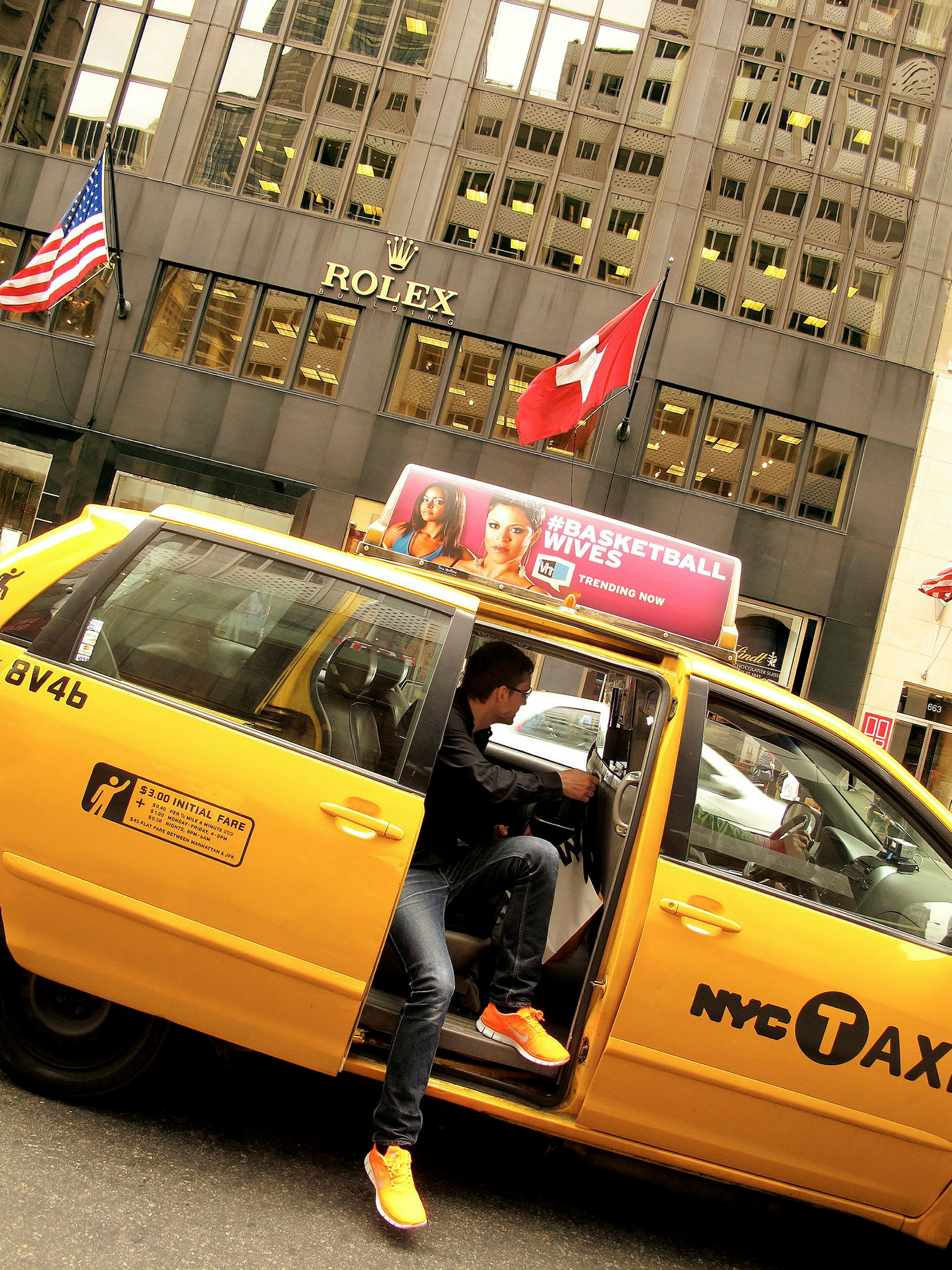 En gul taxi parkert foran en bygning med Rolex-logoen og to flagg, det amerikanske og det sveitsiske. (AI-generert tekst)