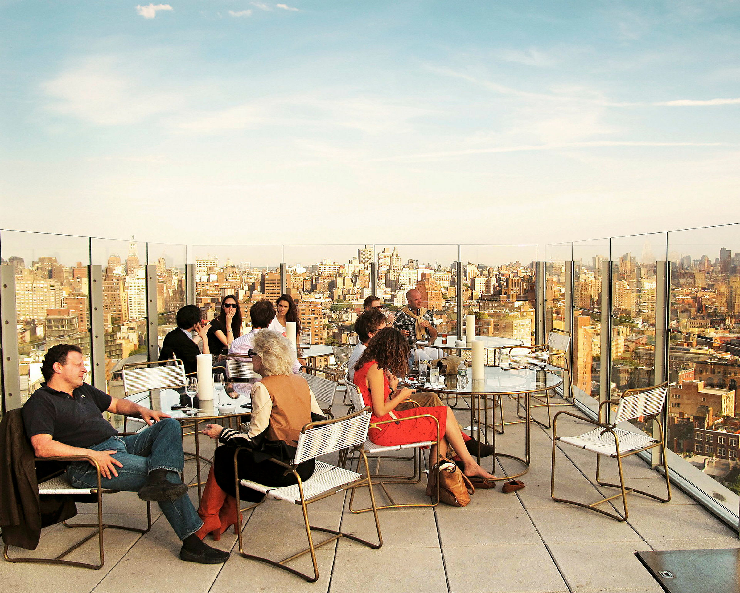 Personer som sitter ved bord på en takterrasse med utsikt over en by i bakgrunnen. (AI-generert tekst)