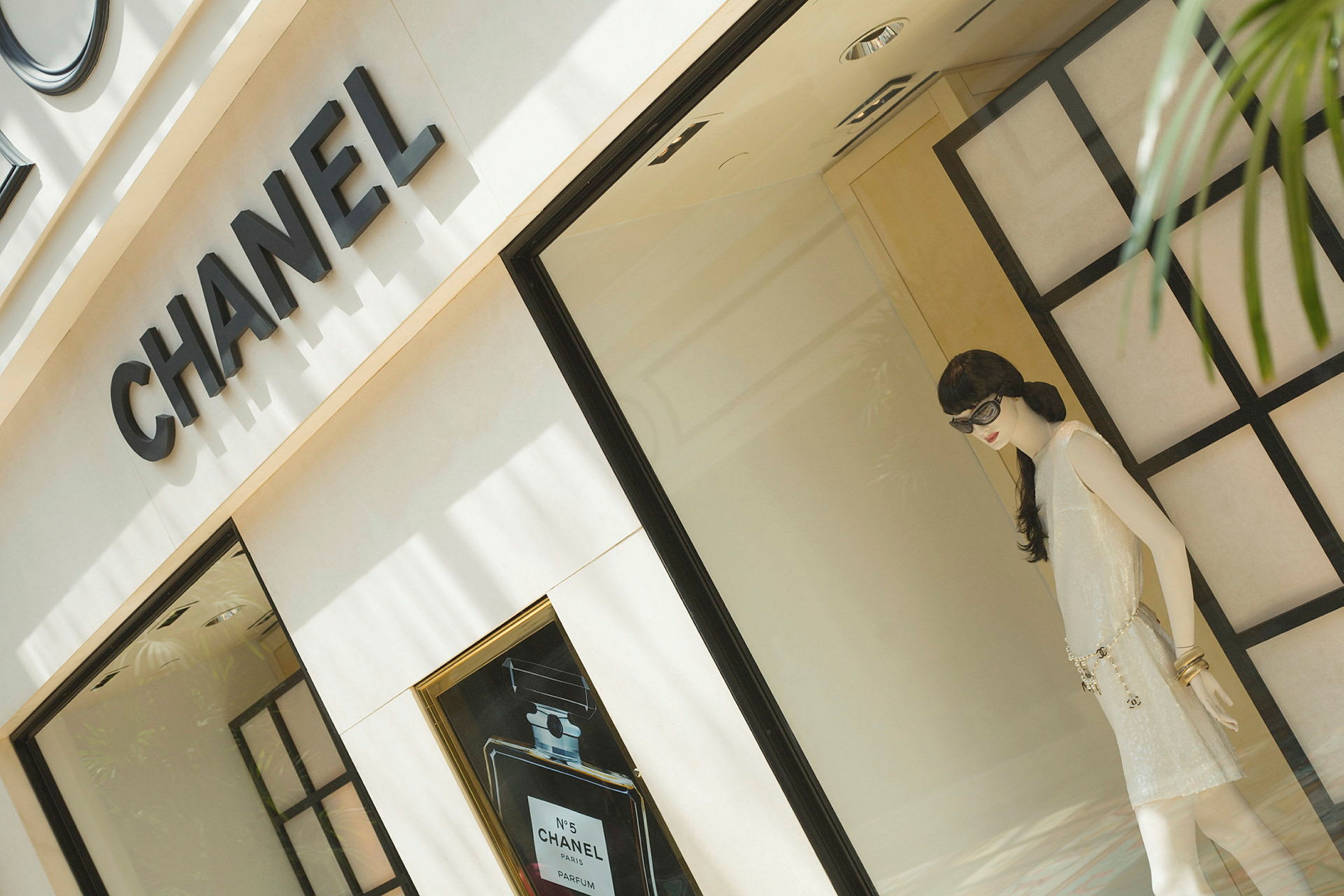 Et utstillingsvindu tilhørende en Chanel-butikk, inneholdende en dukke i en elegant bekledning. (AI-generert tekst)