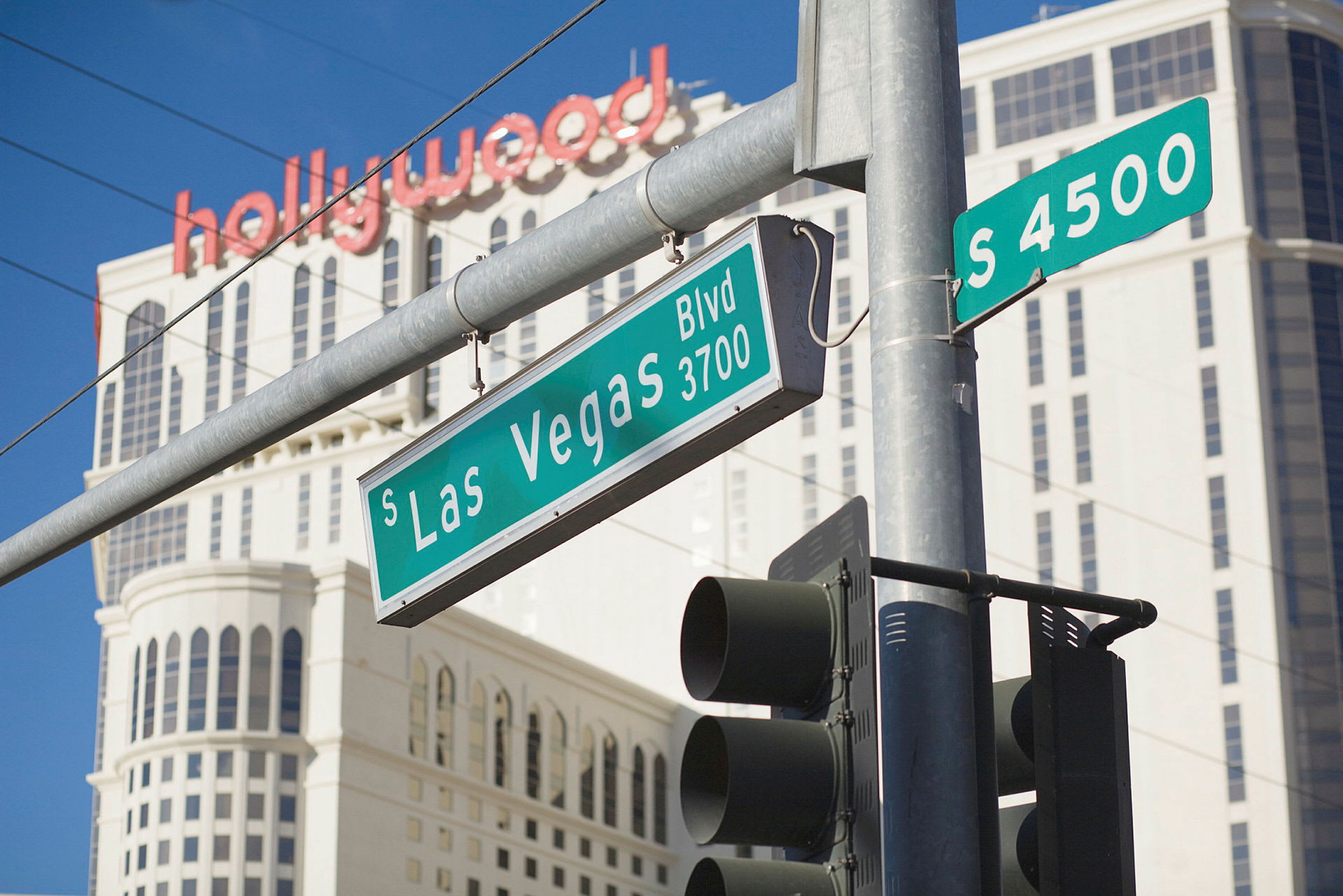 Fotgjengerfelt med trafikklys og gateskilt ved South Las Vegas Boulevard, med en høy bygning og teksten "hollywood" i bakgrunnen. (AI-generert tekst)