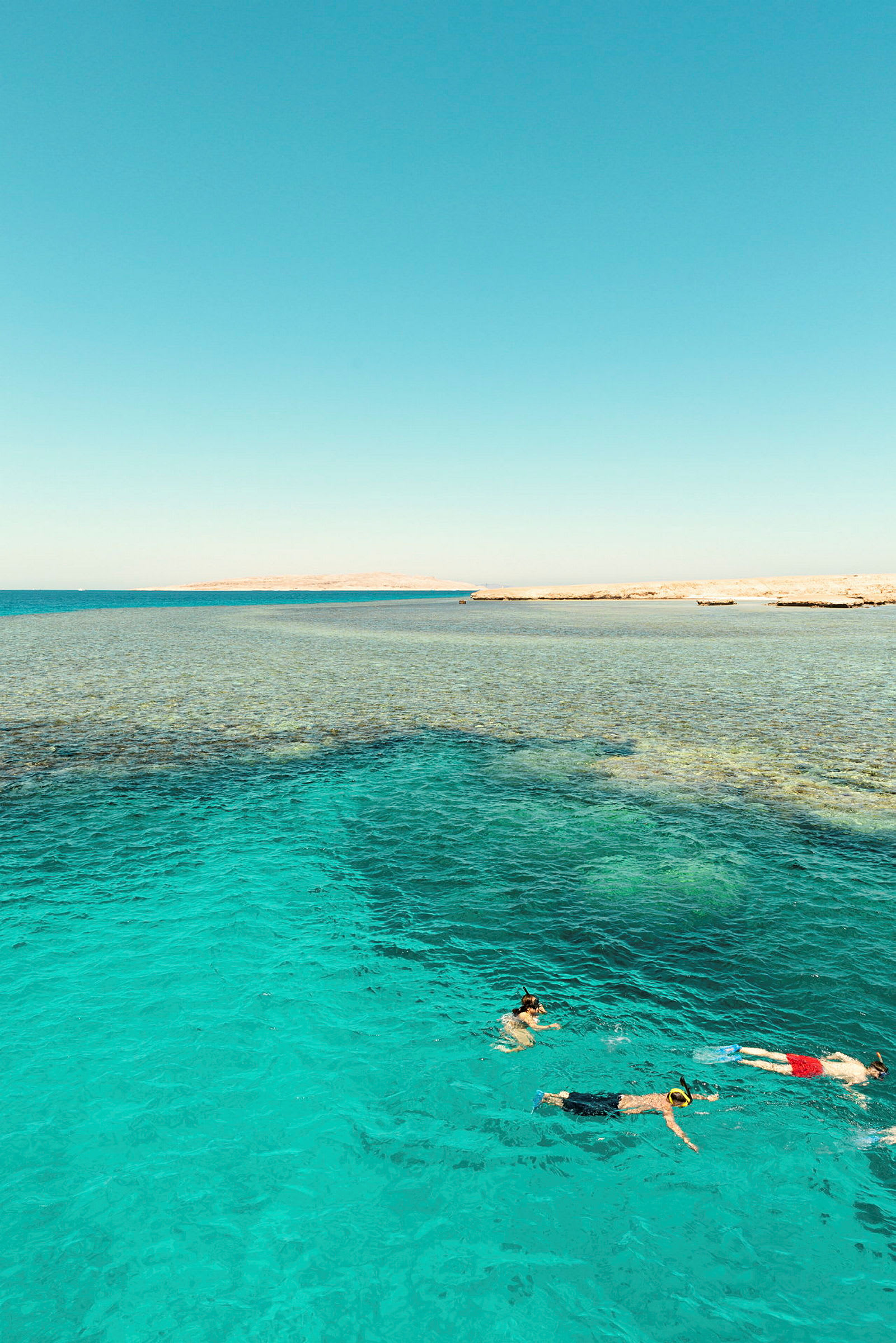 Bildet viser tre personer som snorkler i klart turkis vann nær en strand. (AI-generert tekst)