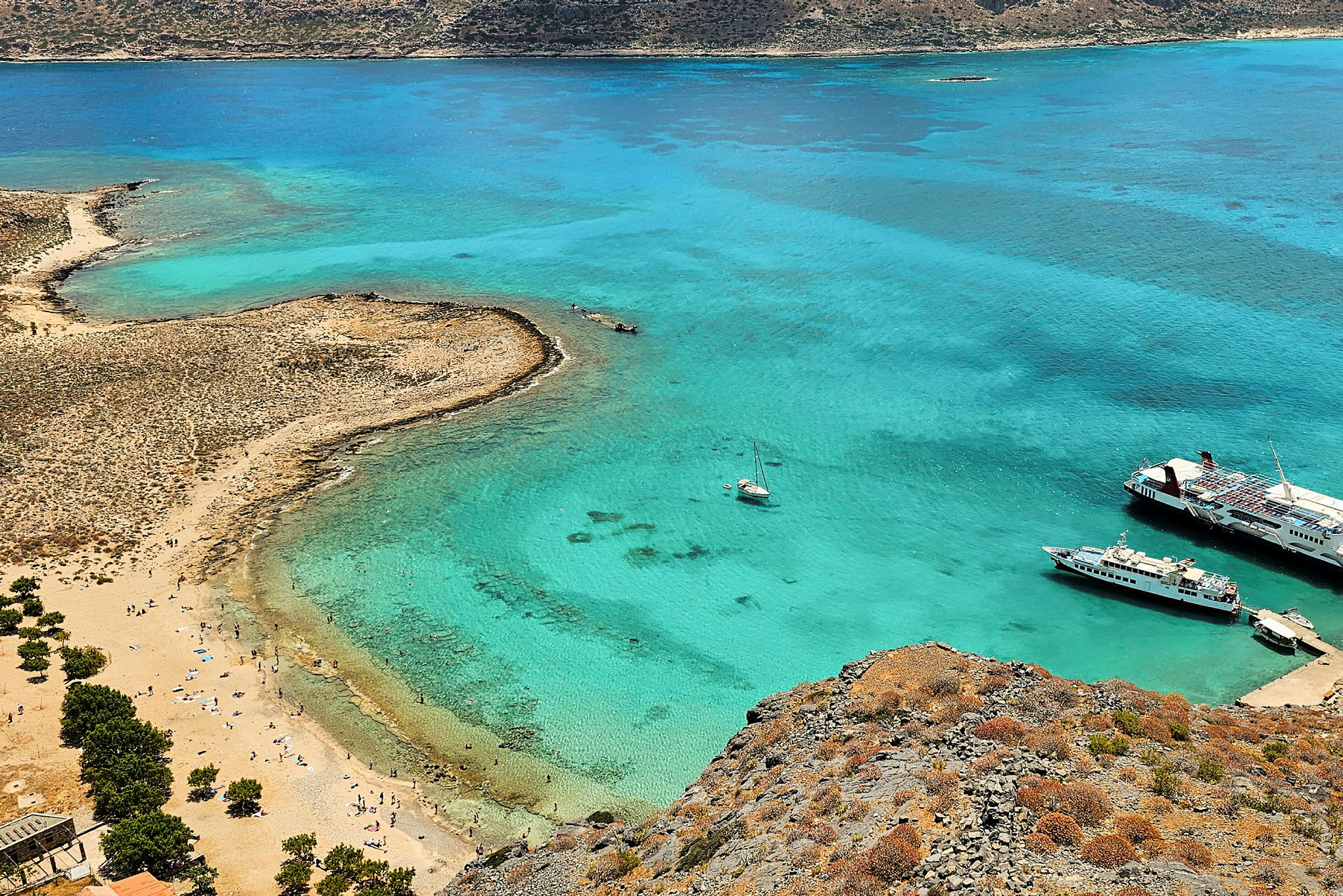 En strand med turkisblått vann. Det er båter i vannet og mennesker på stranden. (AI-generert tekst)