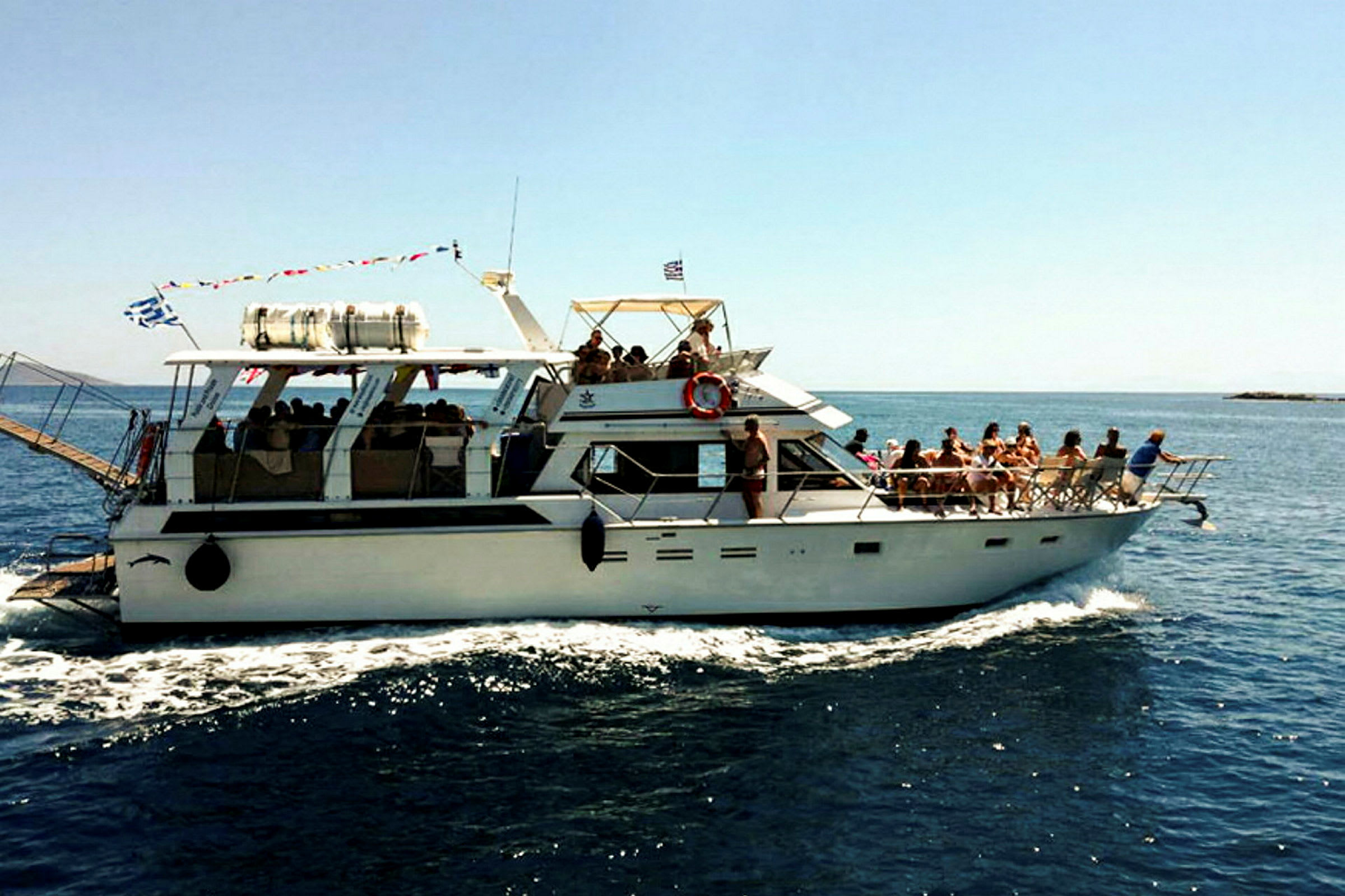 En motorbåt med mennesker om bord beveger seg på havet. Himmelen er klar og blå. (AI-generert tekst)