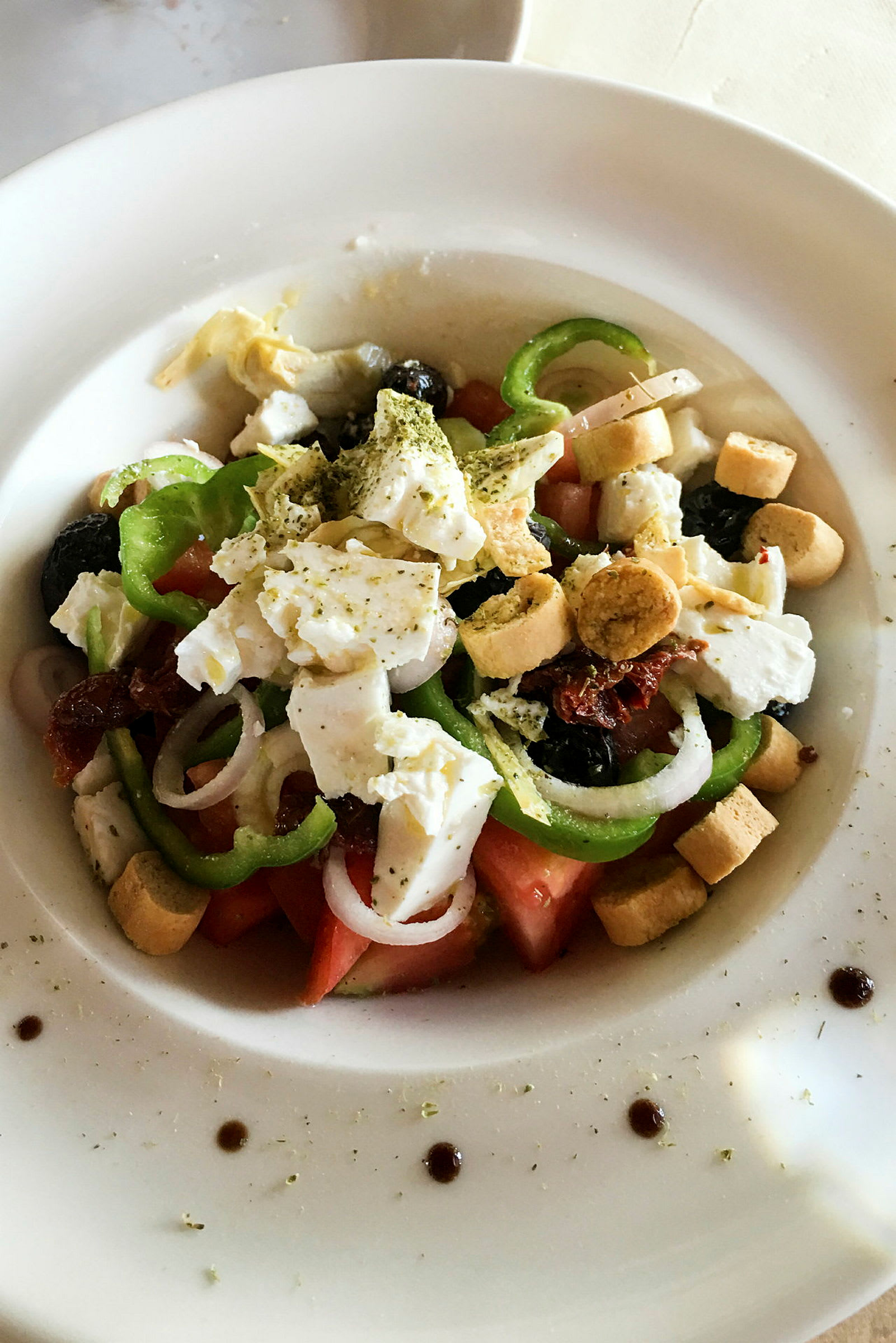 En tallerken med salat som inneholder tomat, paprika, løk, fetaost, oliven og krutonger. (AI-generert tekst)