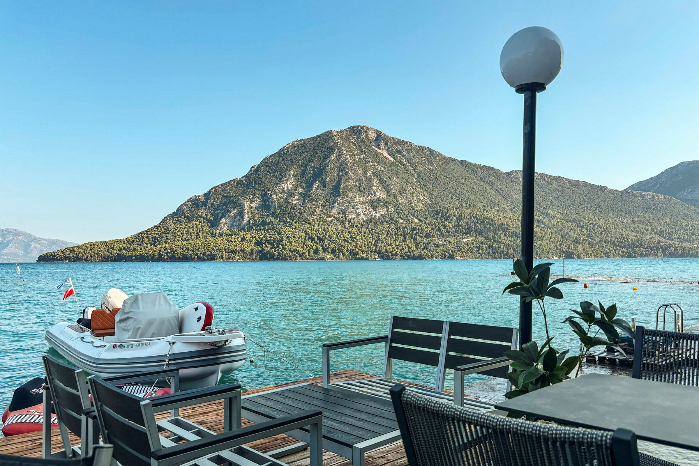 Et bord med stoler ved en brygge med utsikt over havet og en grønnkledd fjellknaus. (AI-generert tekst)