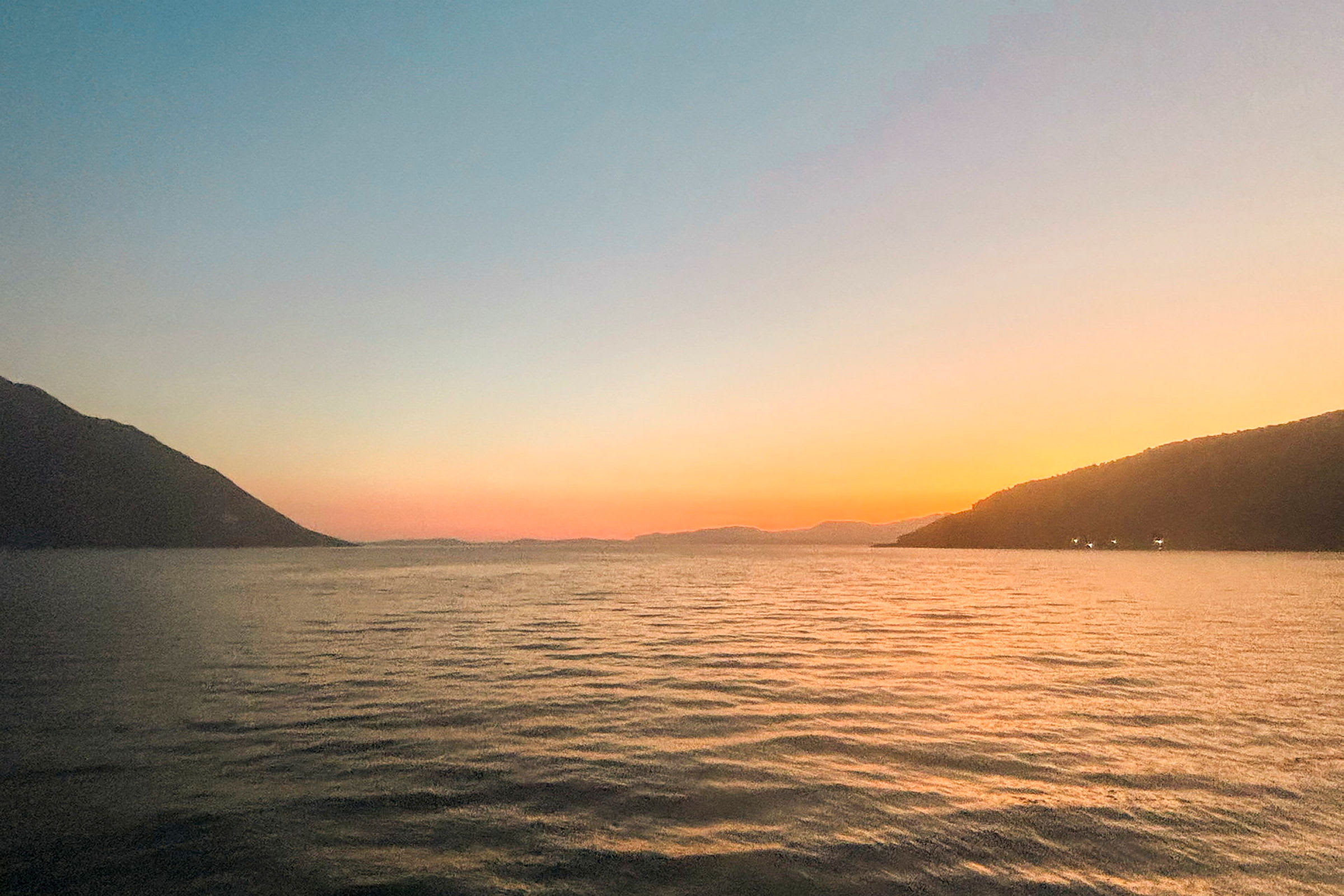 Solnedgang over et rolig hav med fjell i det fjerne. (AI-generert tekst)