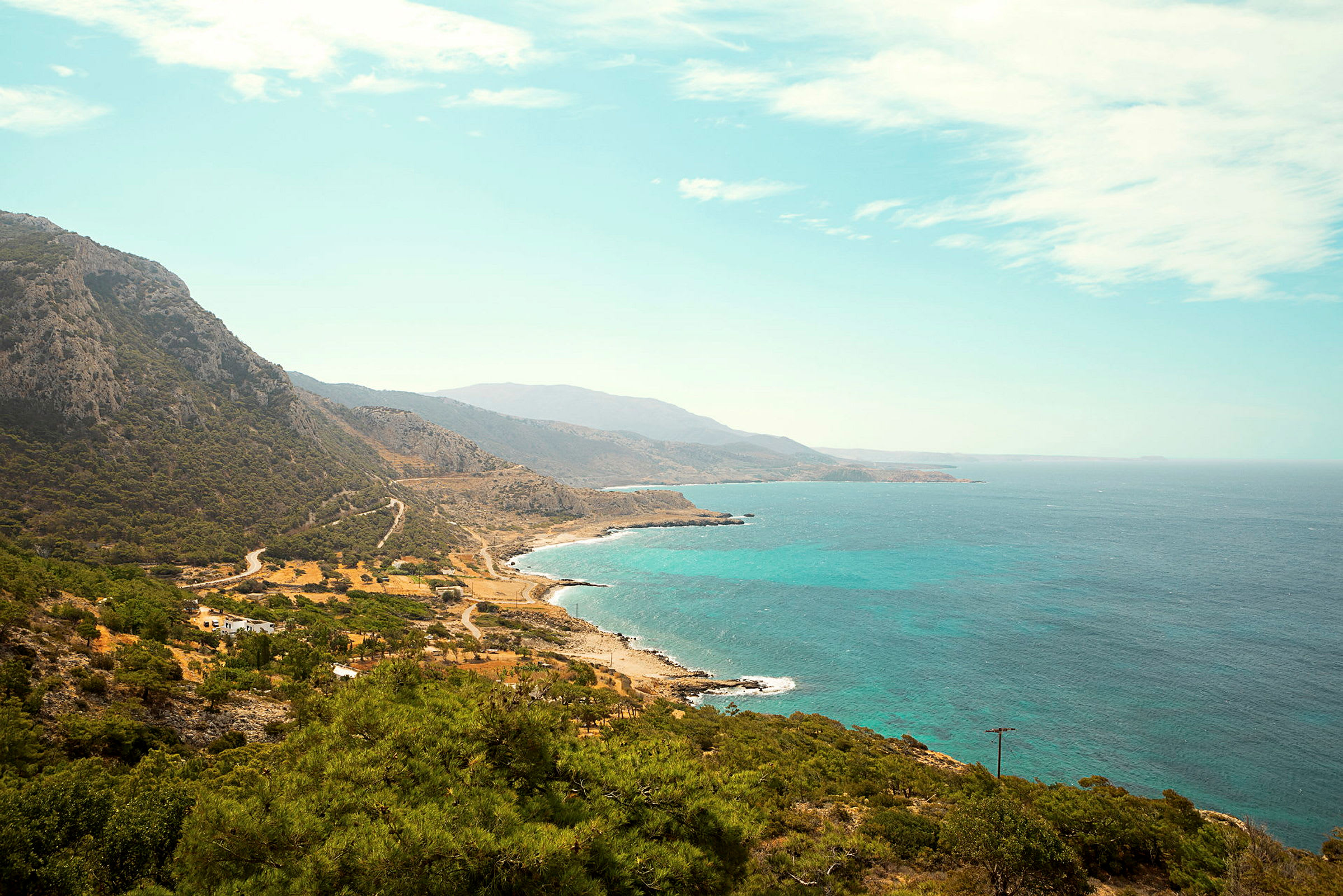 Et kystlandskap med et fjellområde som strekker seg mot havet, der turkist vann møter en klar himmel. (AI-generert tekst)