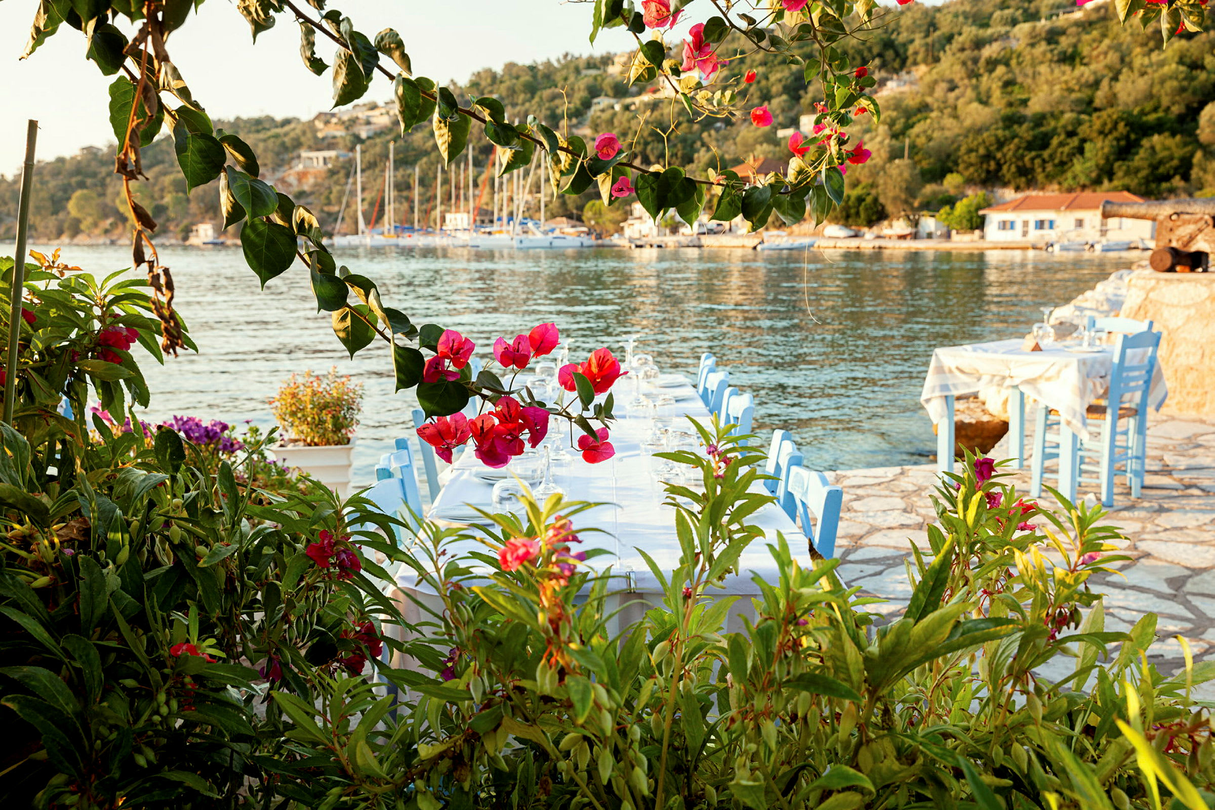 Restaurantbord ved stranden med utsikt over havet og omgitt av blomster. (AI-generert tekst)