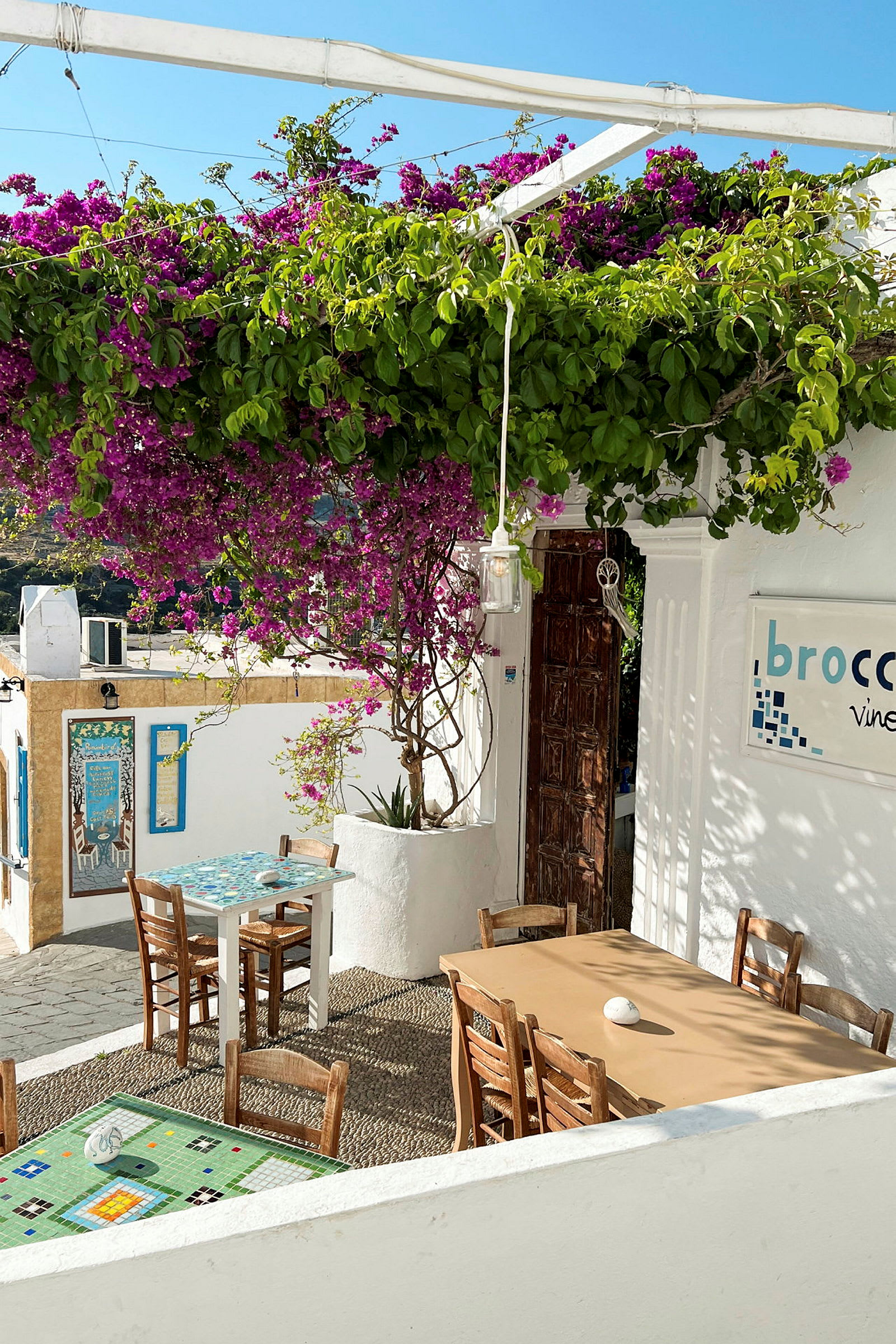 Utendørsområde av en restaurant med bord og stoler under en blomstrende pergola. (AI-generert tekst)