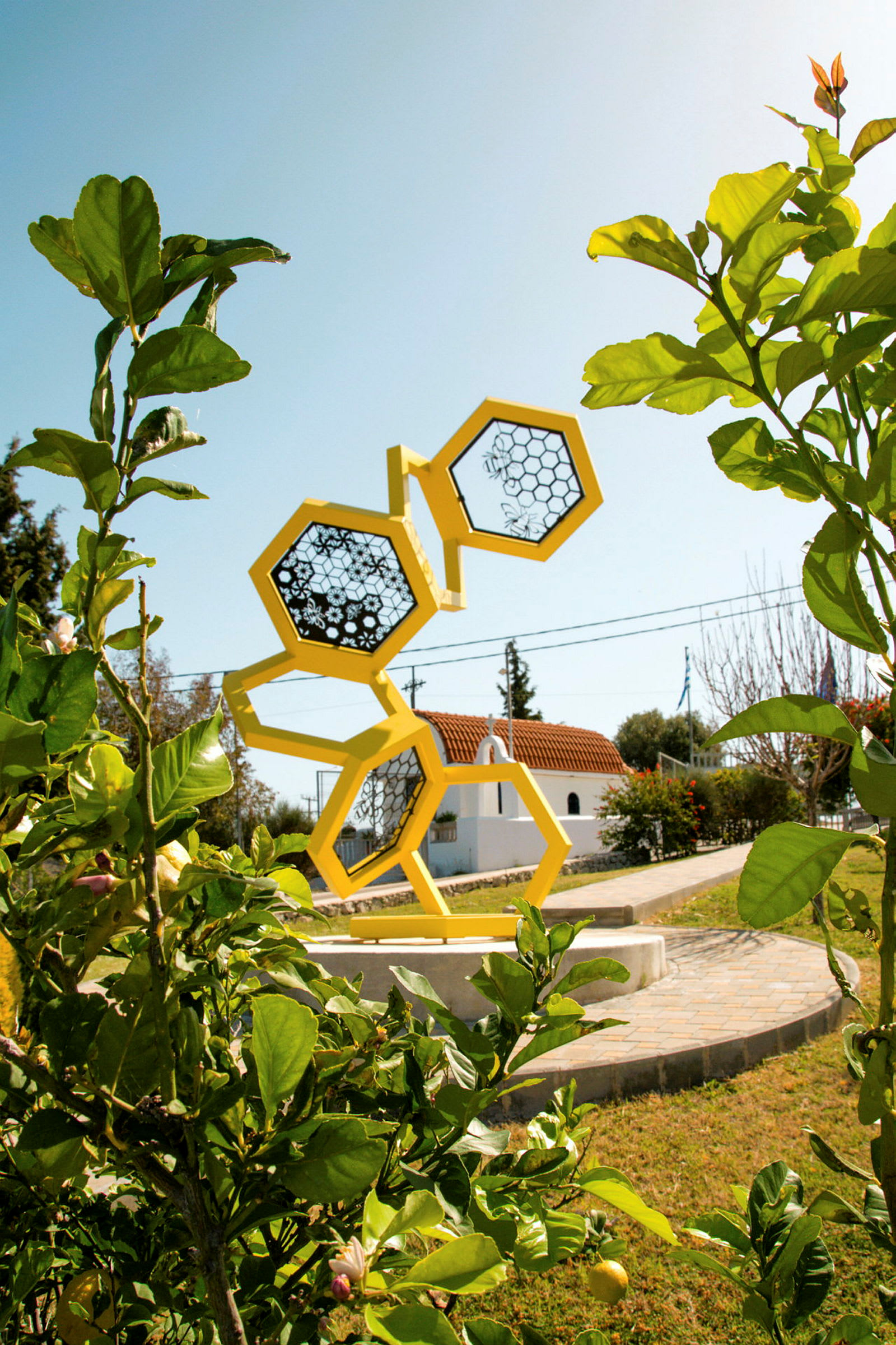 En skulptur av gule heksagoner står i en hage med grønt omkring. (AI-generert tekst)