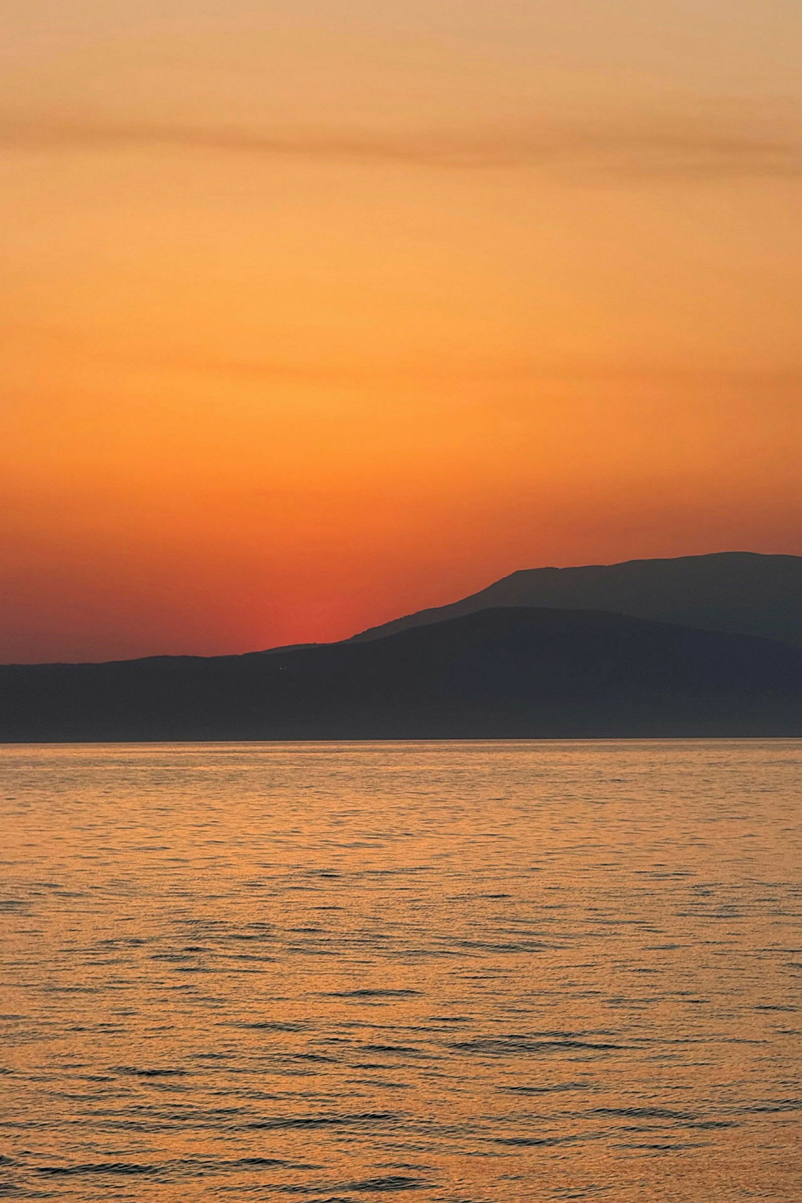 Solnedgang over havet med silhuetter av fjerne fjell. (AI-generert tekst)