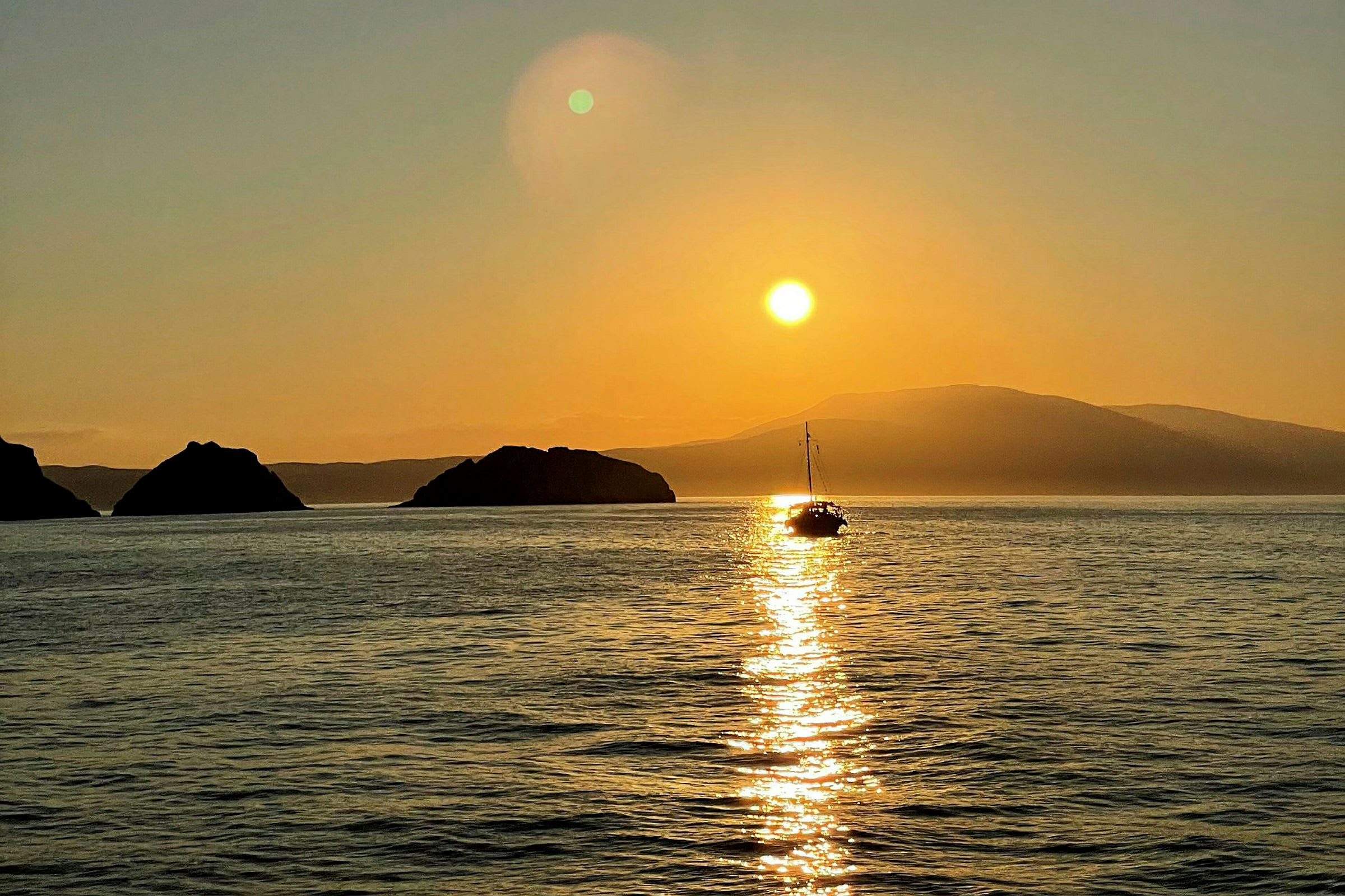 En seilbåt på havet ved solnedgang, med fjell i bakgrunnen. (AI-generert tekst)