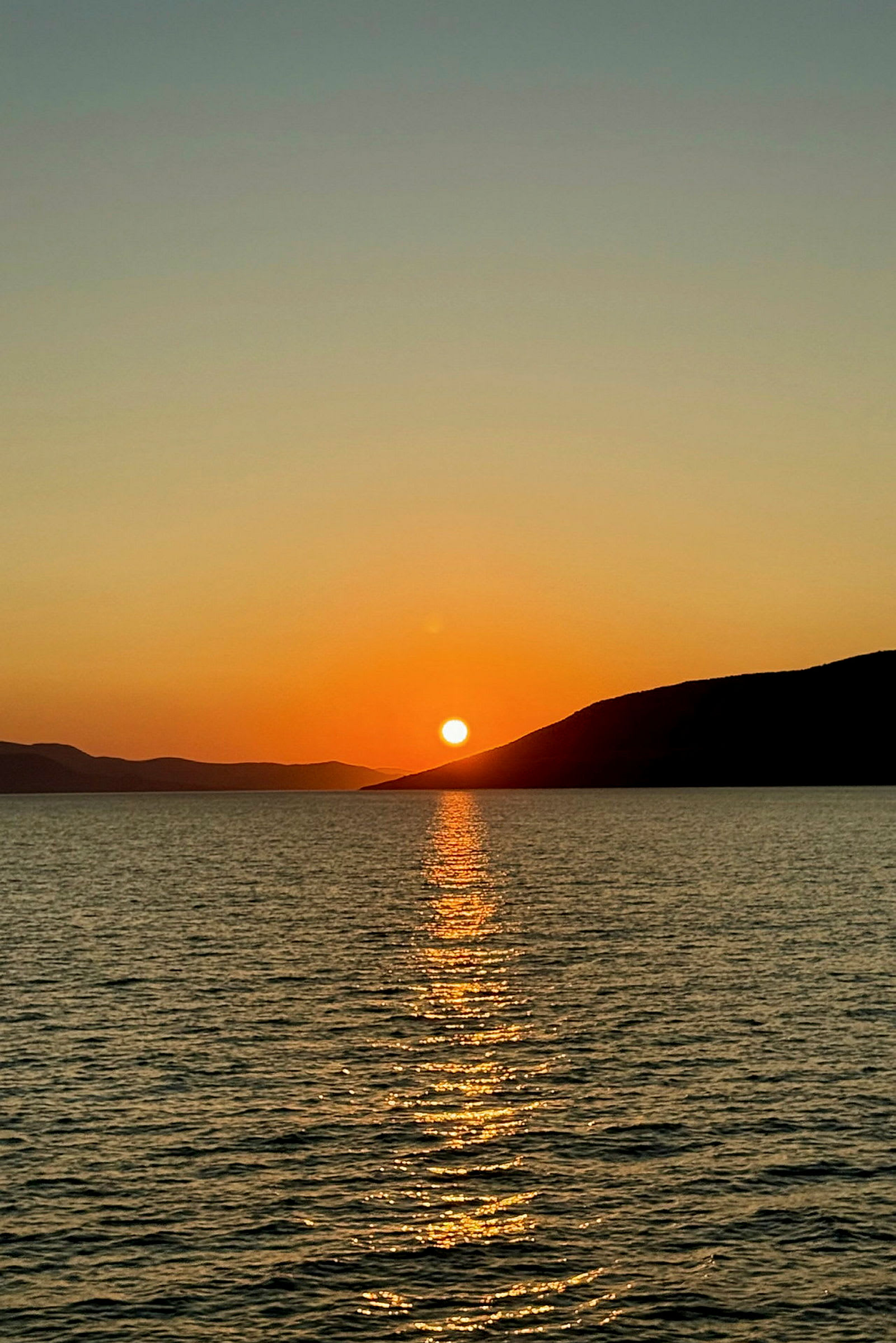 Bilde av en solnedgang over havet med speilinger i vannet og fjell i bakgrunnen. (AI-generert tekst)